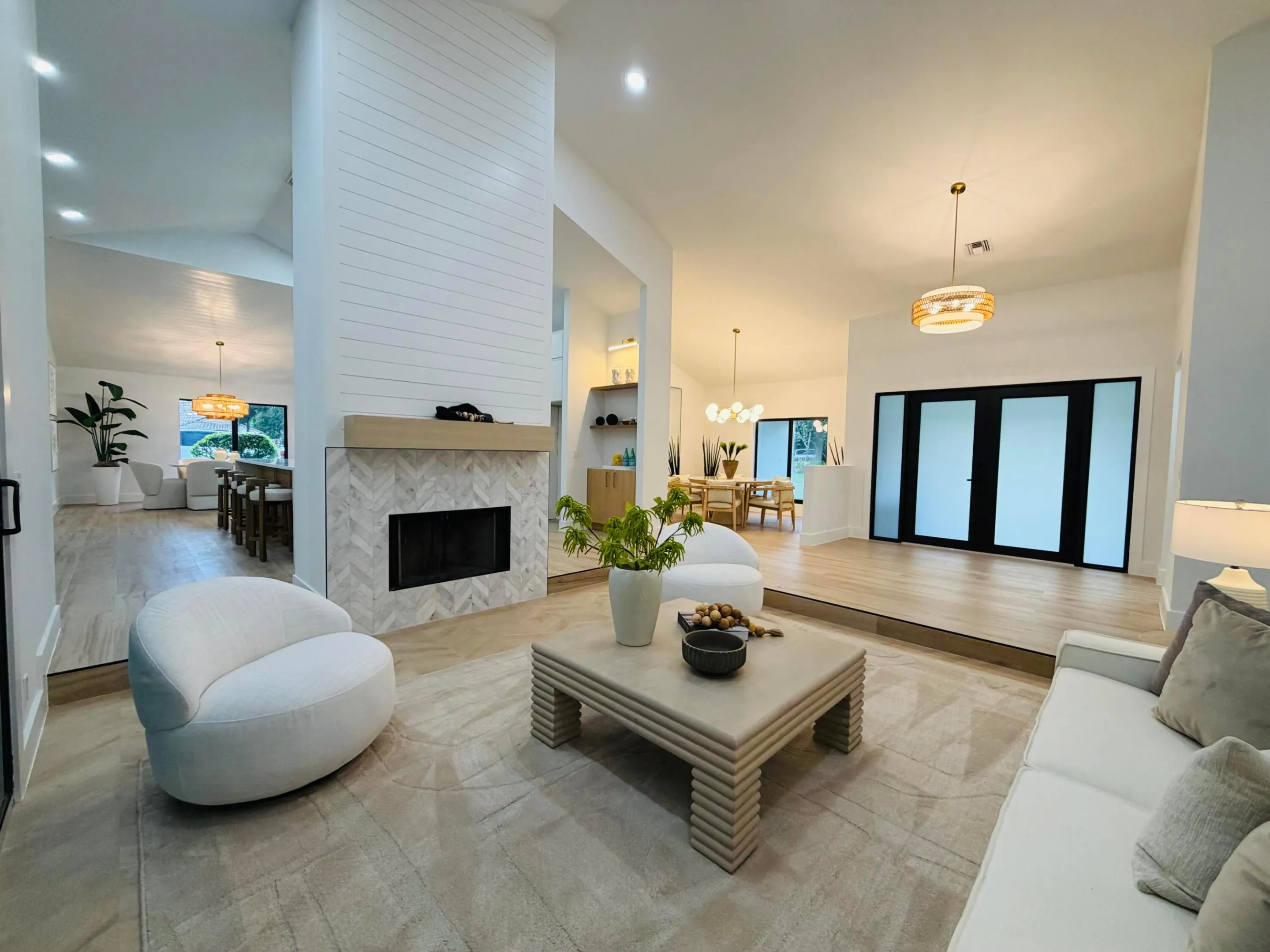Vaulted ceilings, wood-finish flooring, a contemporary fireplace with a herringbone tile surround, and an entry with double frosted glass doors