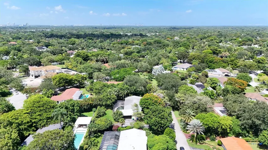 Wide aerial shot capturing the neighborhood's lush greenery and the home's prime setting.