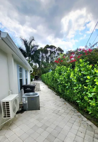 Paver pathway alongside a lush green hedge and flowering shrubs