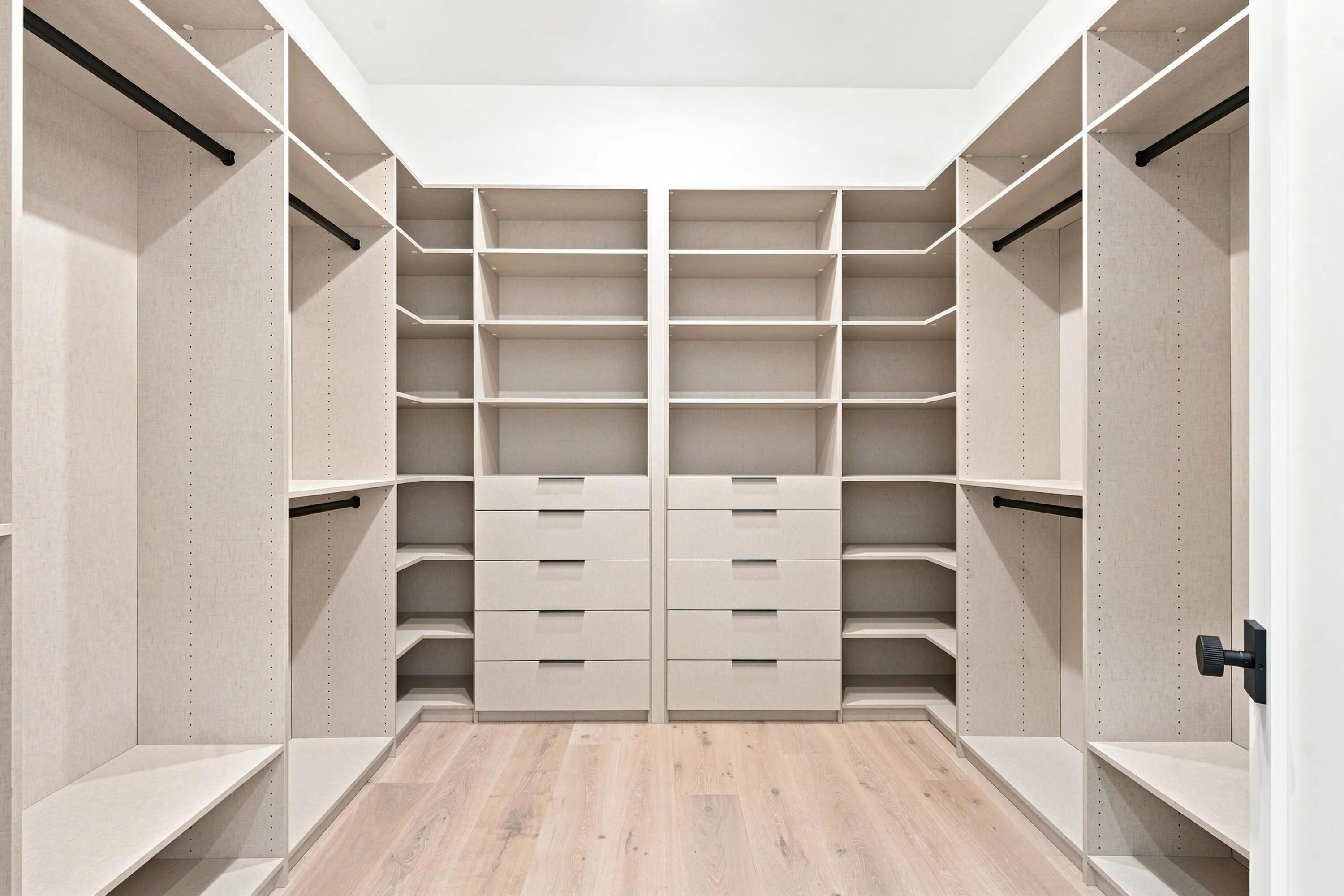 Custom closet system with multiple shelving units, hanging rods, built-in drawers, and light wood-finish flooring