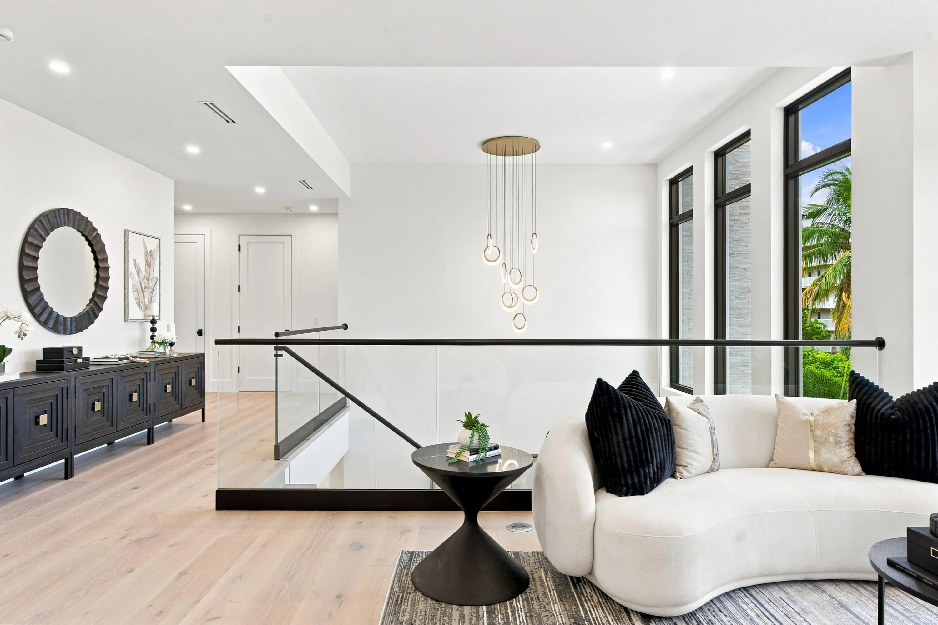 High ceilings with recessed lighting, wood-finish flooring, glass and metal railing, multiple large windows, and a contemporary chandelier
