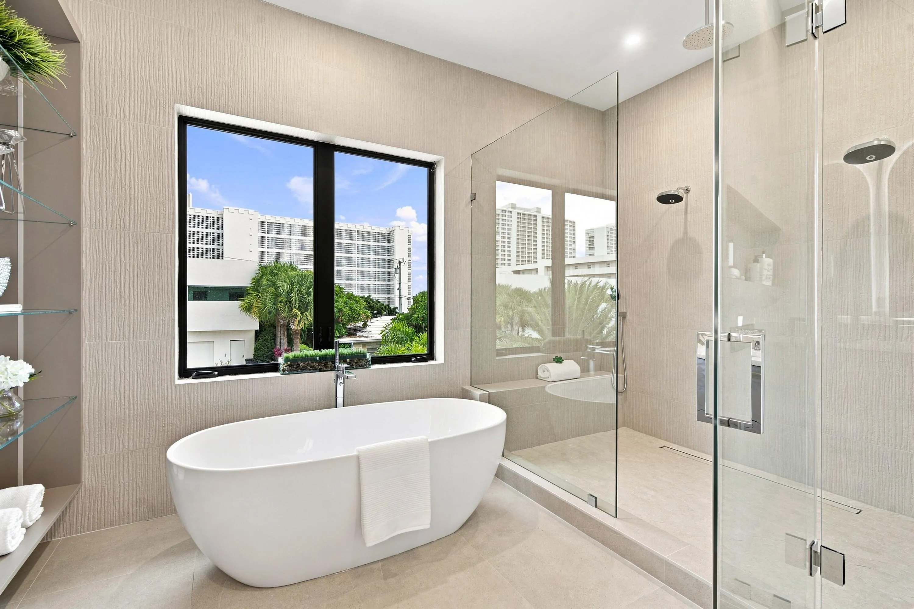 Freestanding oval soaking tub, glass-enclosed shower with dual shower heads, large window, and built-in glass shelving
