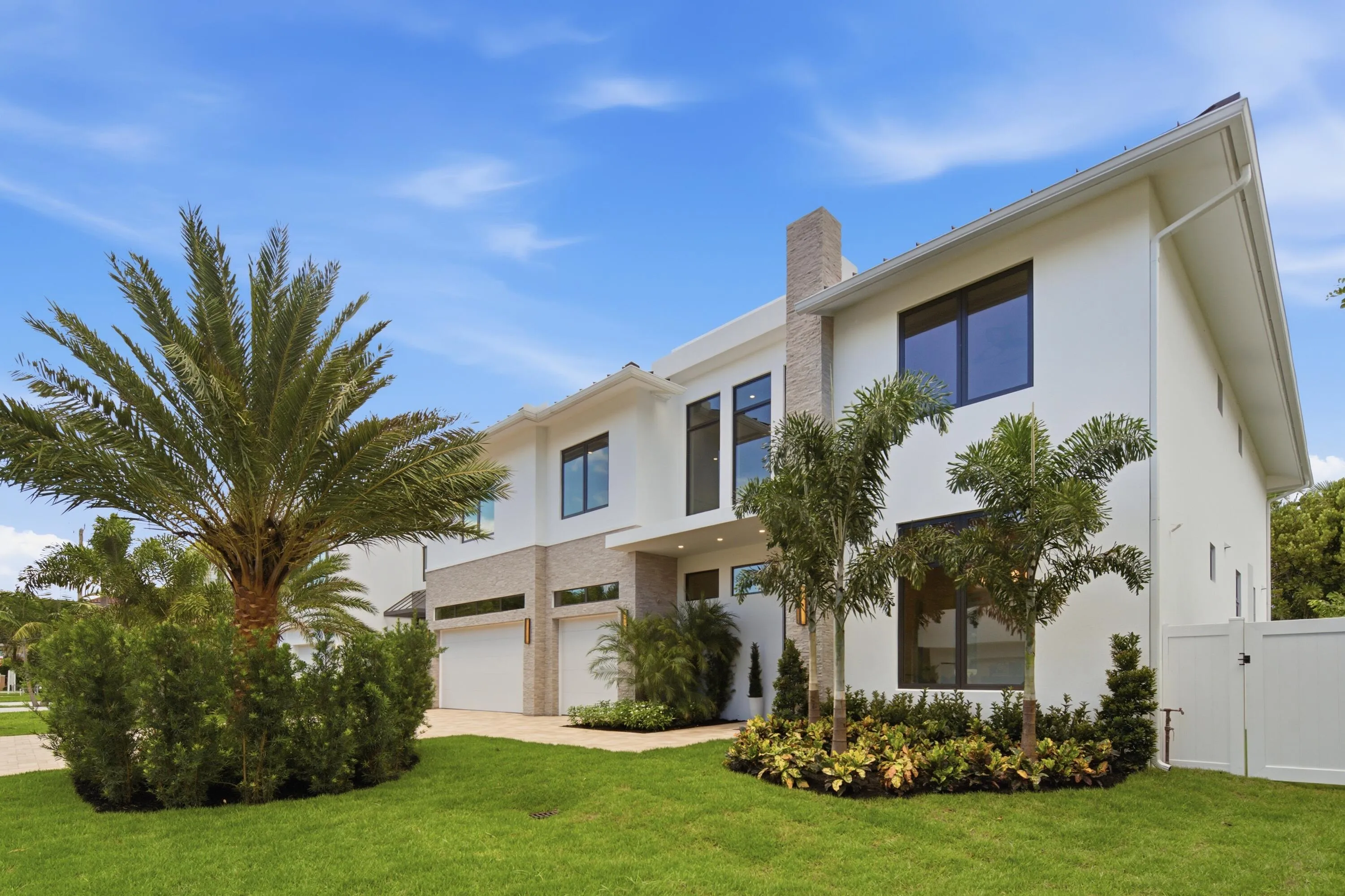Modern white stucco exterior with a stone-clad chimney, dark-framed windows, and multiple garage doors