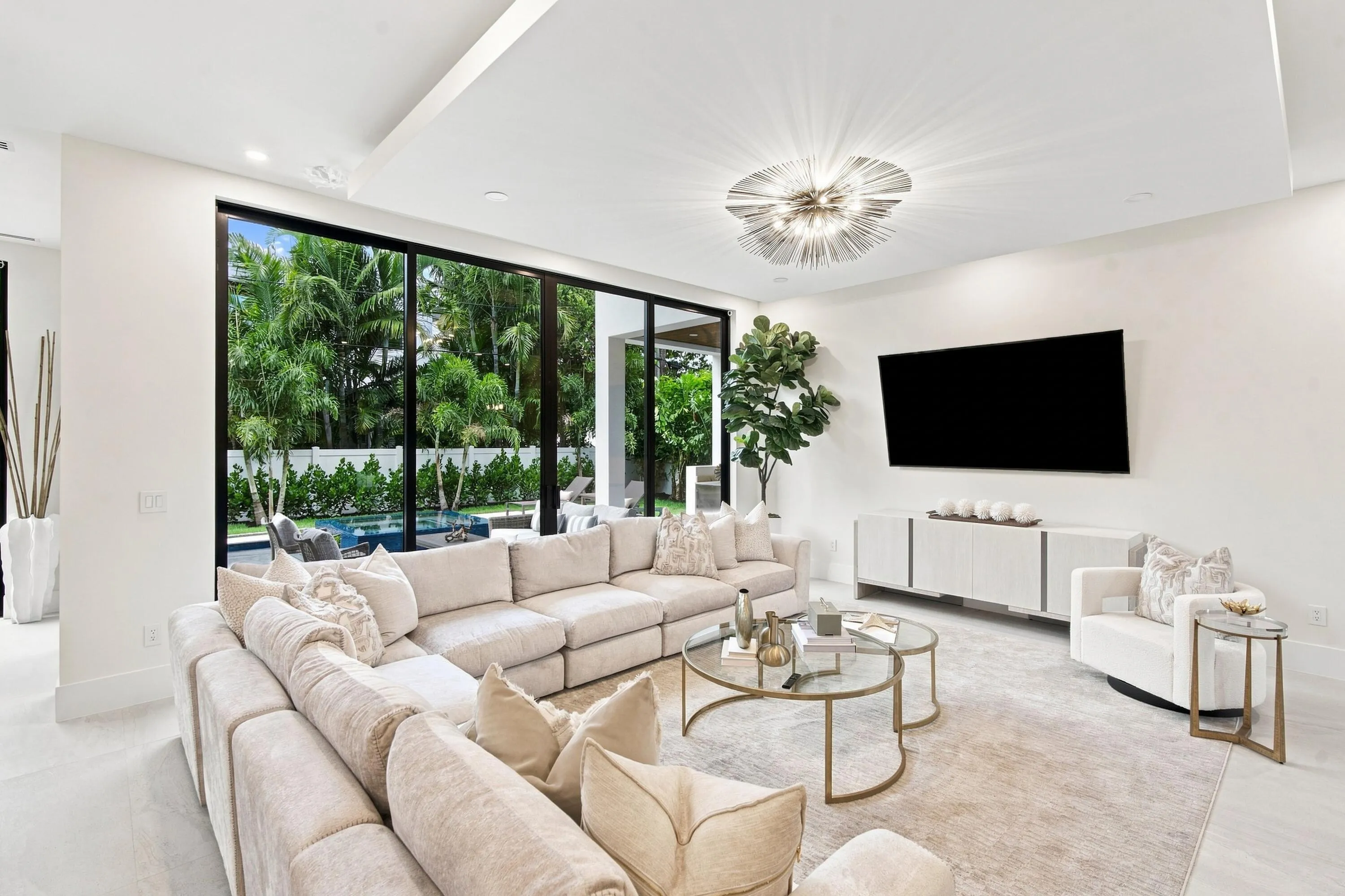 Modern living space featuring expansive floor-to-ceiling windows, a recessed ceiling, an ornate light fixture, and a built-in media console