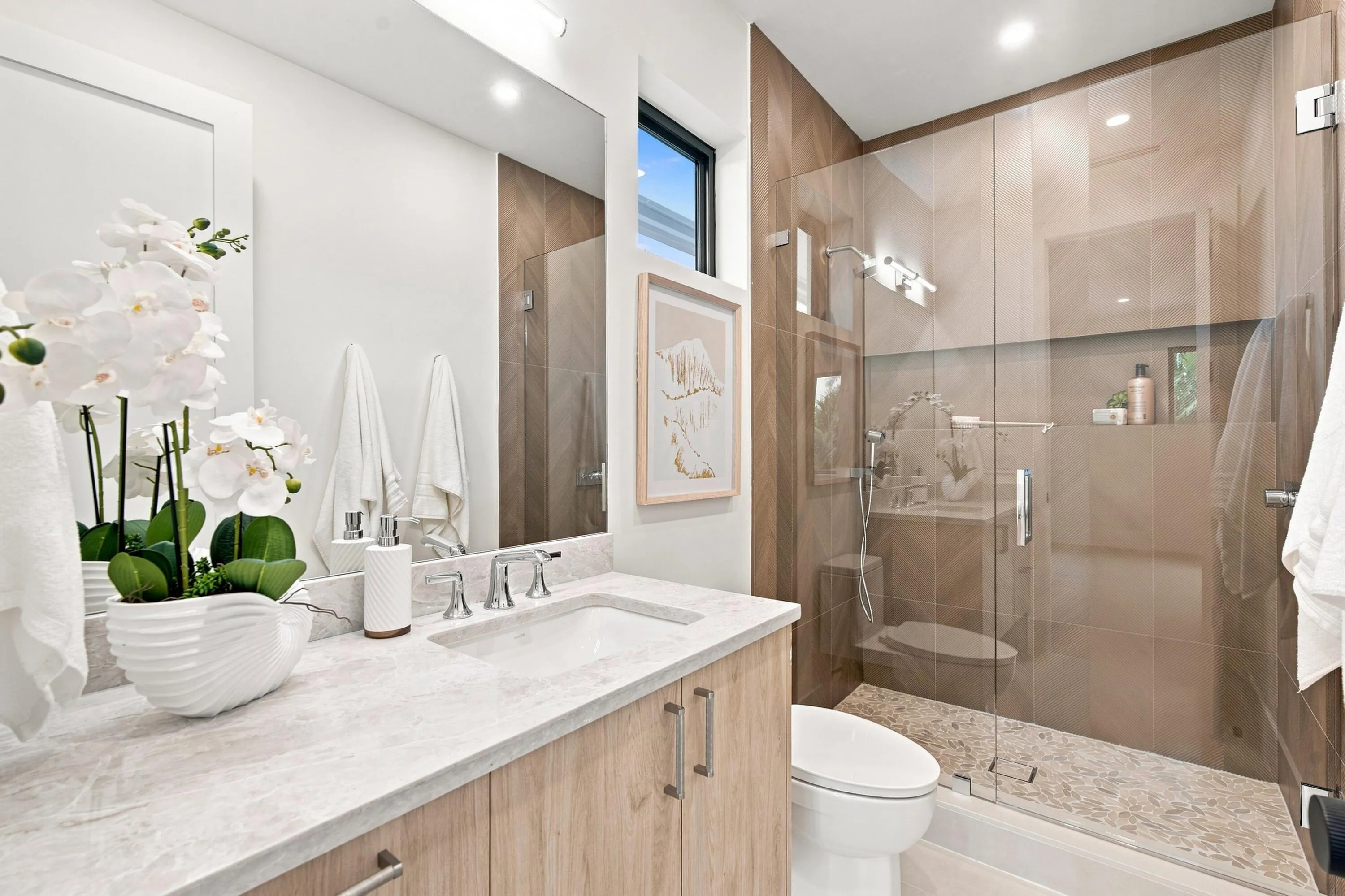 Modern vanity with light-toned cabinetry and a light-toned countertop, paired with a frameless glass shower enclosure featuring large-format wall tiles and a pebble-finish shower floor