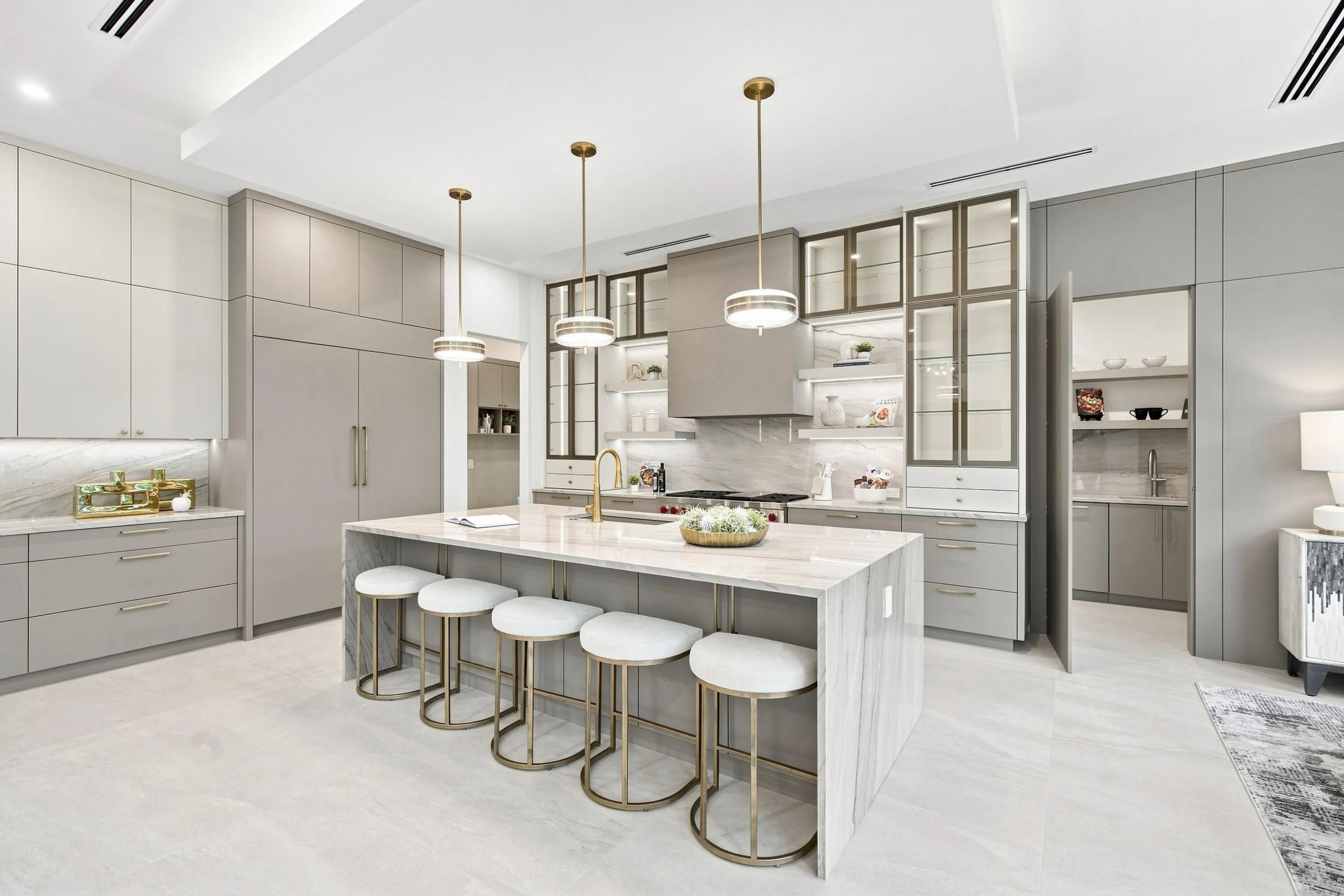 Expansive kitchen with a waterfall edge island, custom cabinetry, integrated appliances, decorative pendant lighting, and a walk-in pantry