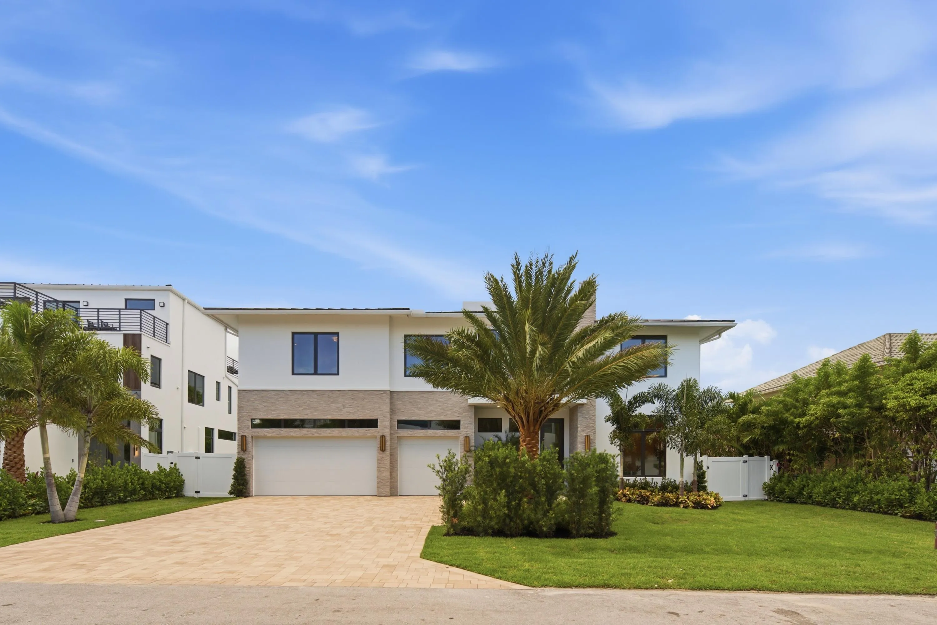 Contemporary two-story residence featuring a paver driveway, three garage bays, and a well-maintained lawn