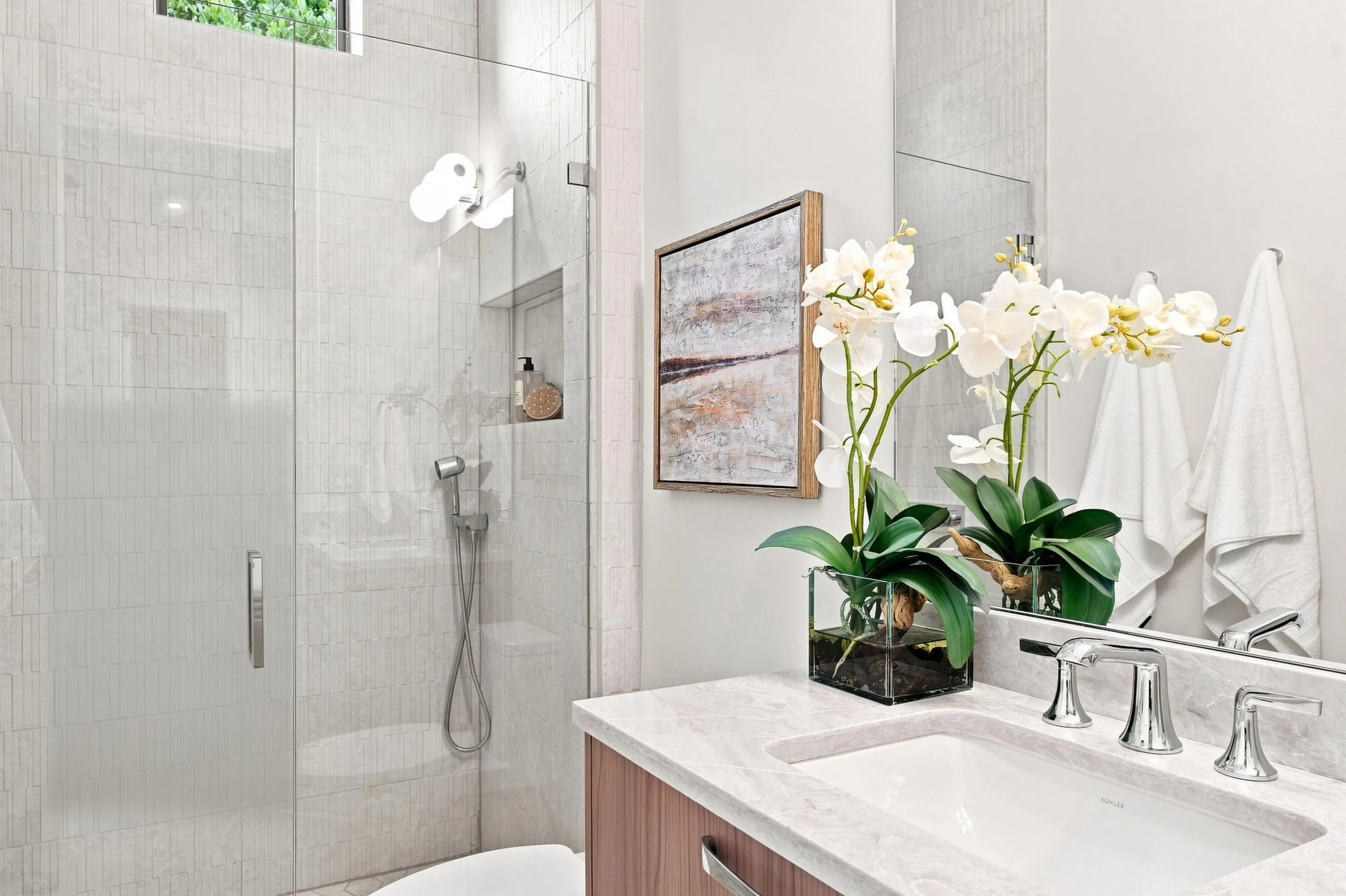 Glass-enclosed shower with a built-in niche, light-toned tilework, wood-finish vanity, and a large mirror
