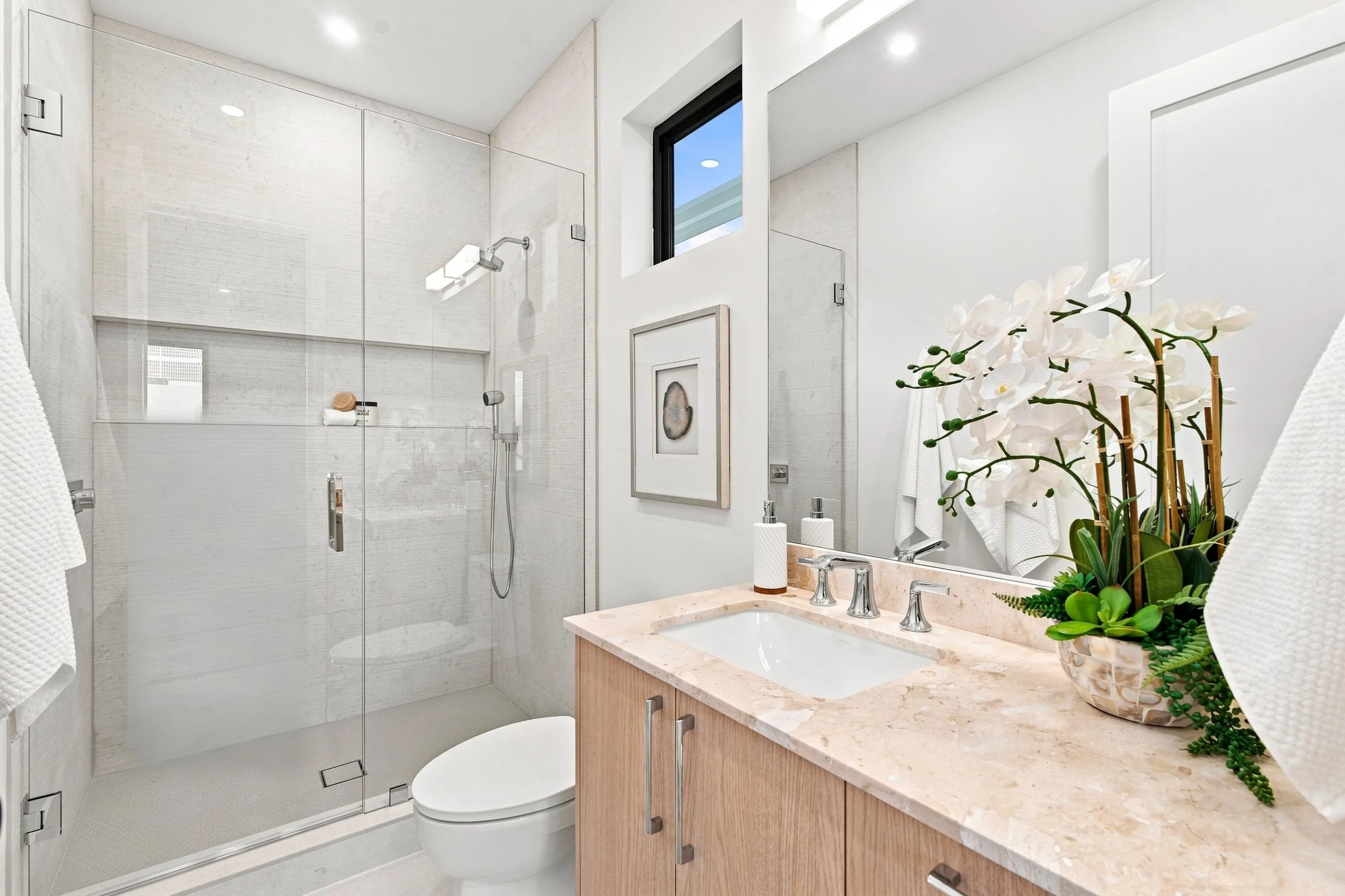 Glass-enclosed shower with a built-in niche, wood-finish vanity with an undermount sink, stone countertop, and a wide mirror