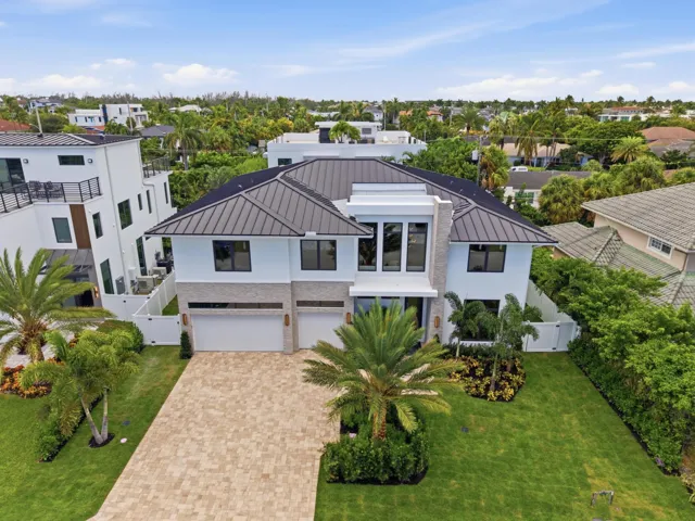 Contemporary architecture featuring a dark metal roof, clean white exterior, and paver driveway