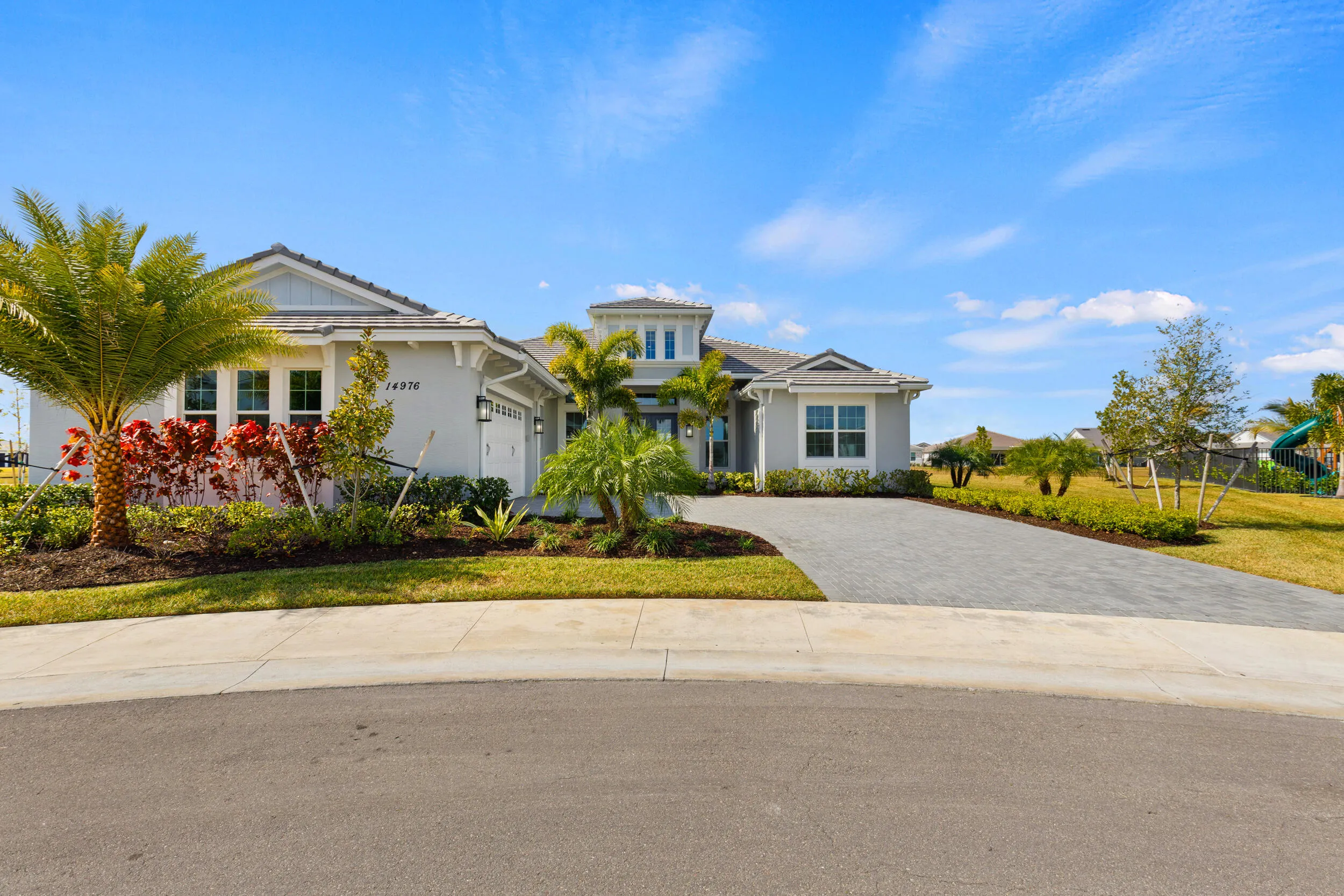 Modern exterior with a light gray facade, decorative shutters, a paved driveway, and mature landscaping