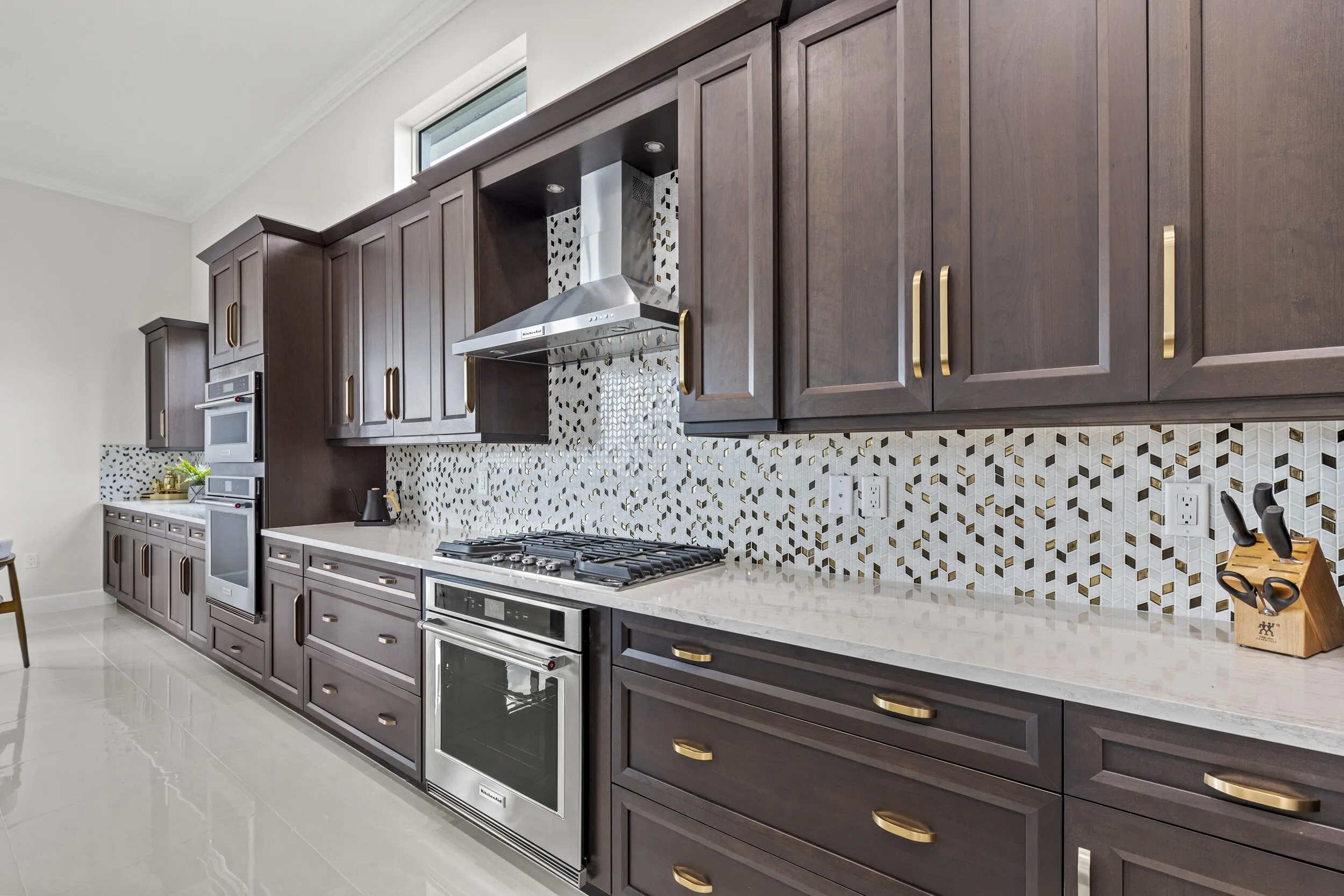 Extensive dark wood-finish cabinetry with gold-tone hardware, light countertops, and a full tile backsplash