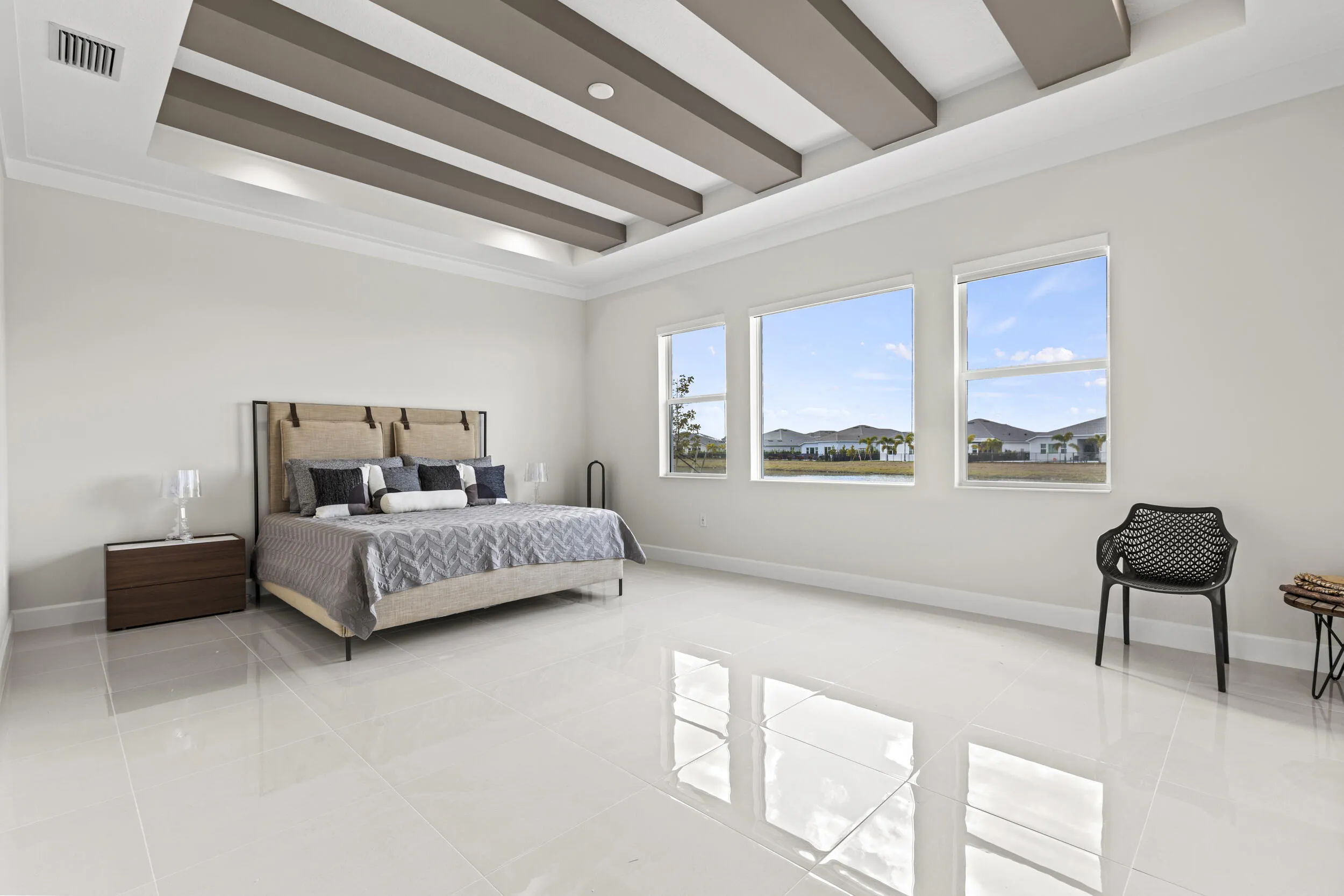 Owner's Suite featuring tray ceiling with decorative beams, large windows, light-toned flooring, and a spacious layout