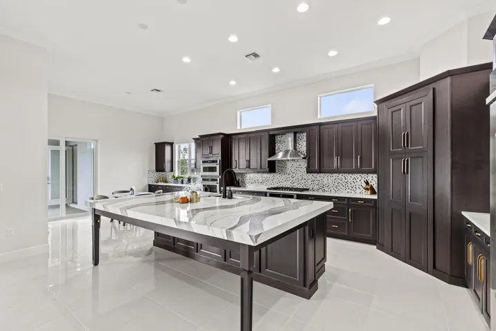 Kitchen featuring dark wood-finish cabinetry, a large center island with a unique veined countertop, mosaic tile backsplash, stainless steel range hood, and recessed lighting