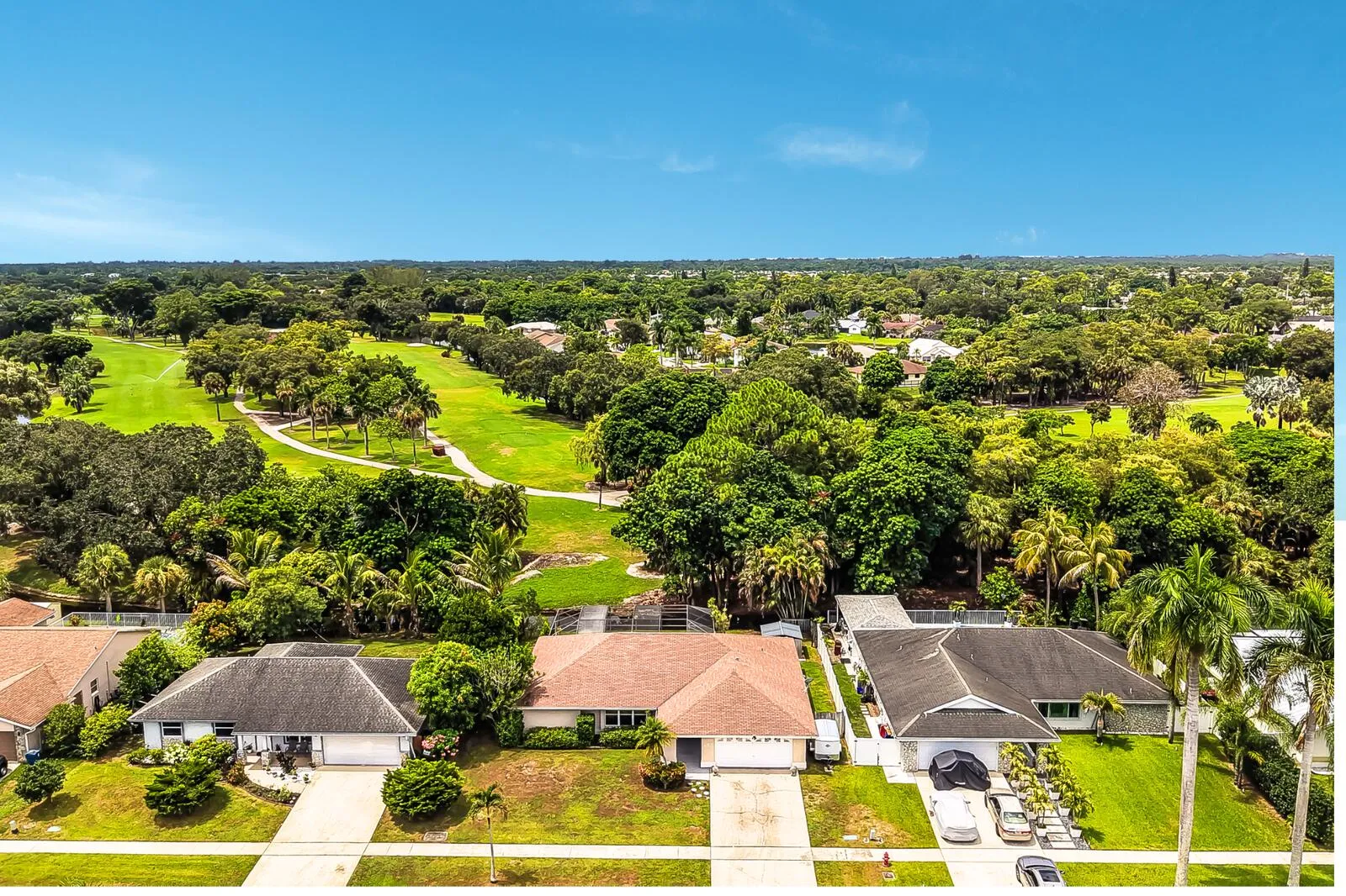 Residences featuring front-facing garages and manicured lawns, situated across from a golf course with mature trees