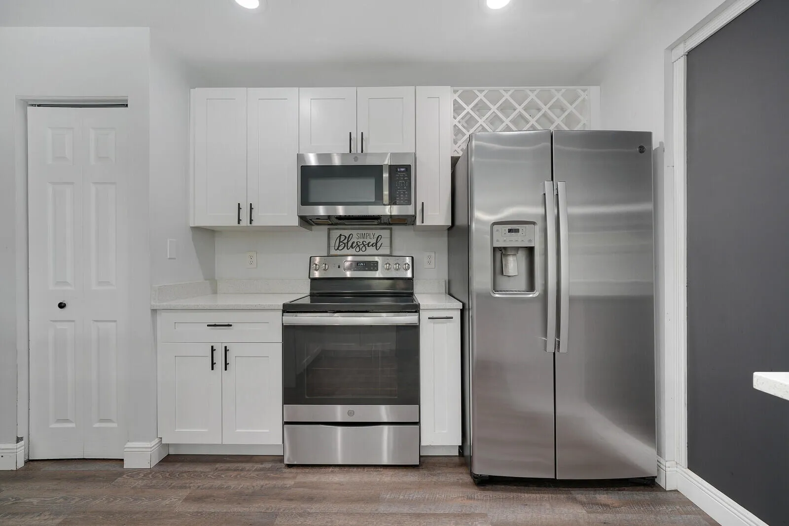 Kitchen featuring white cabinetry, stainless steel appliances, wood-finish flooring, and white countertops