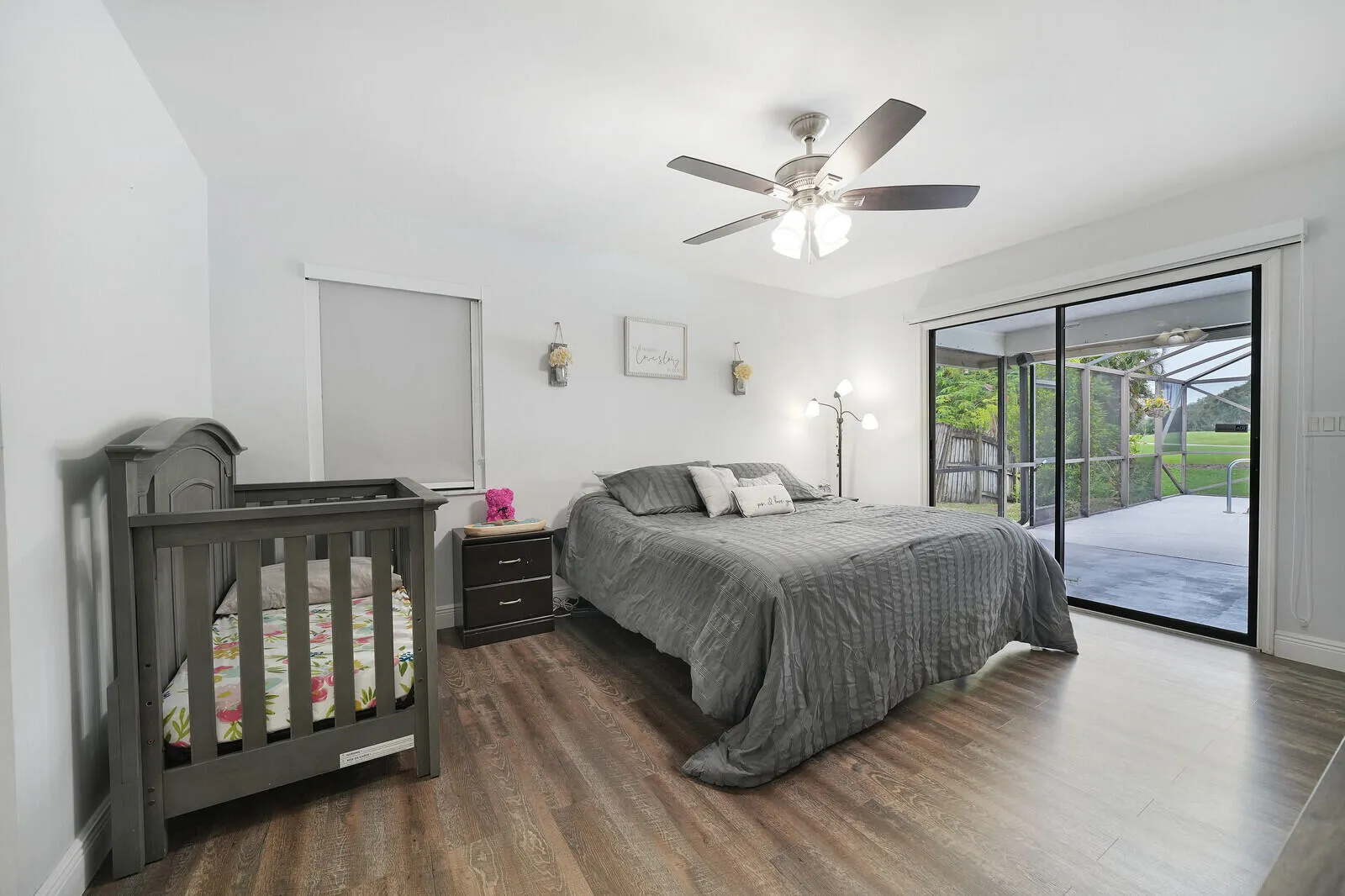 Wood-finish flooring, ceiling fan with integrated lighting, window with roller shade, and sliding glass doors opening to a screened outdoor living area