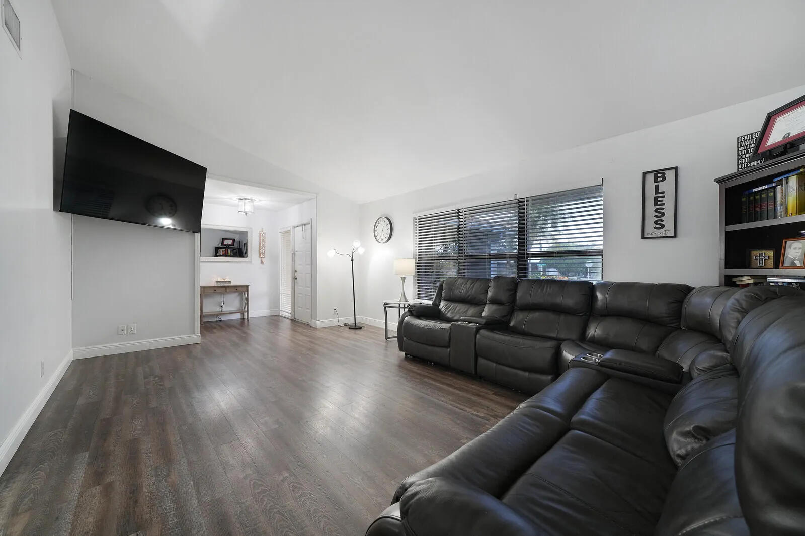 Spacious living area featuring wood-finish flooring, white walls, and multiple windows with blinds