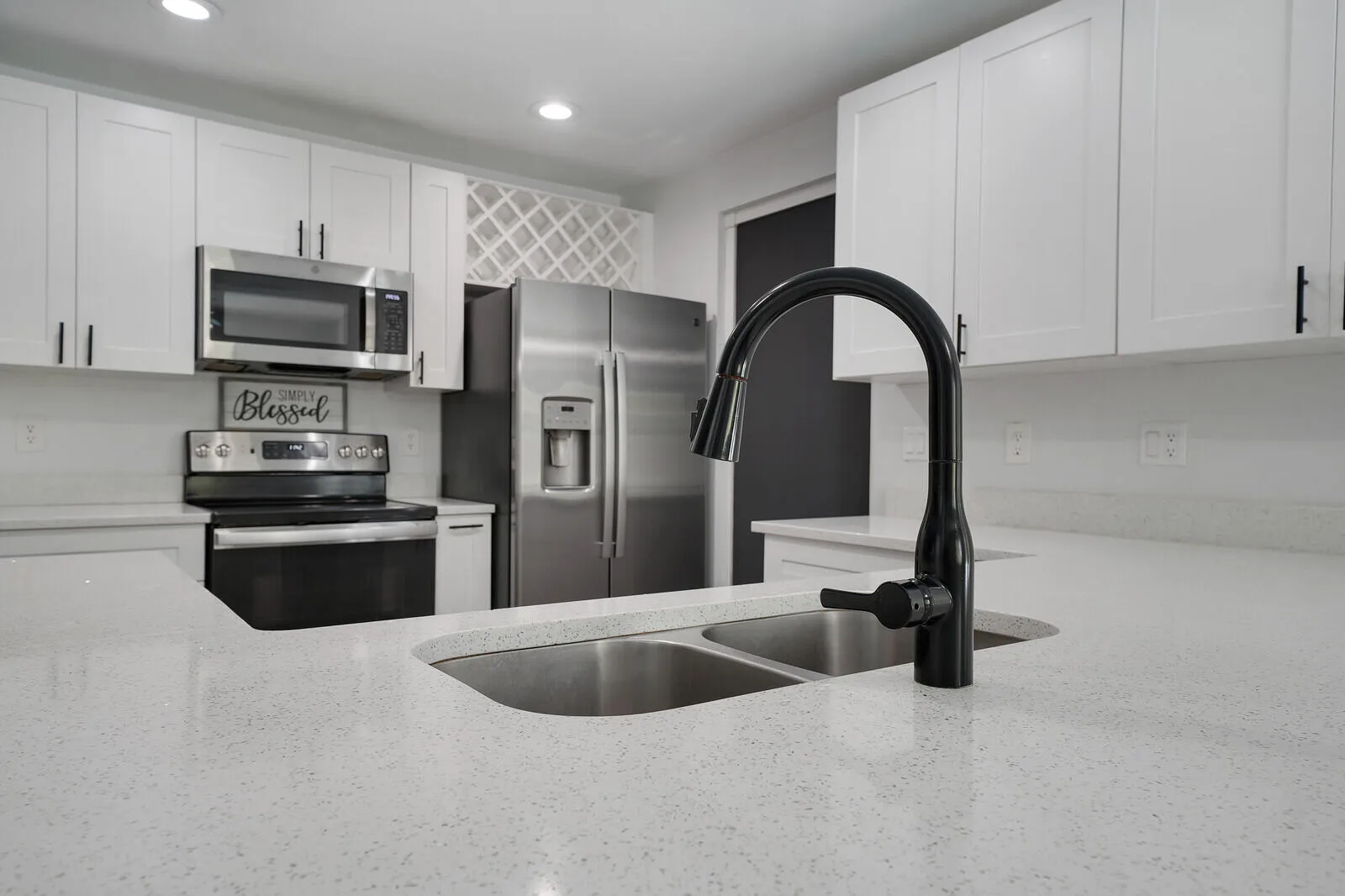 Kitchen featuring white shaker-style cabinetry, light speckled countertops, stainless steel appliances, a built-in wine rack, and a black gooseneck faucet