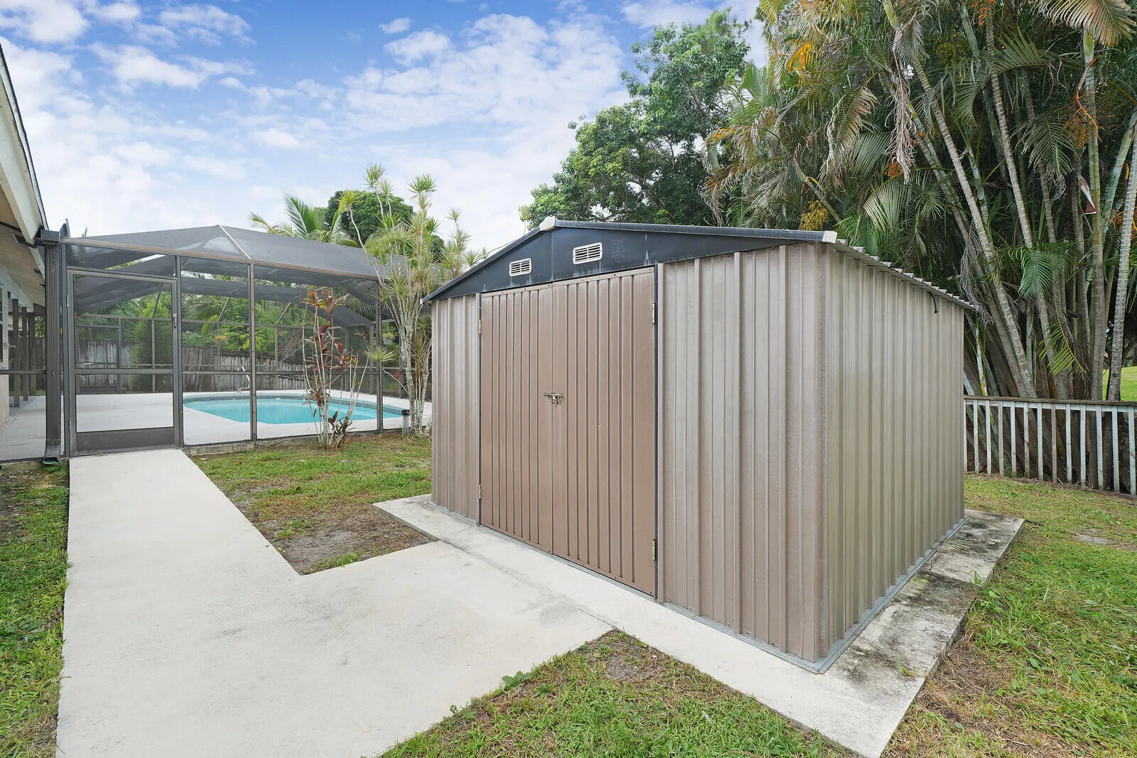 Screened-in pool enclosure, concrete walkways, detached metal storage shed, and mature perimeter landscaping