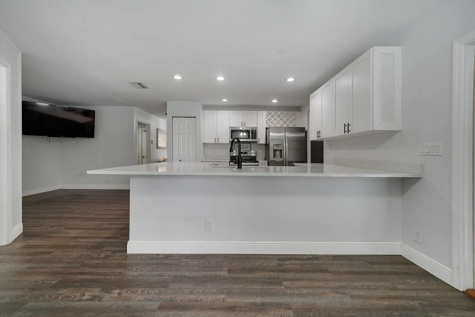 Kitchen featuring white shaker cabinetry, stainless steel appliances, a white countertop island with a breakfast bar, and recessed lighting