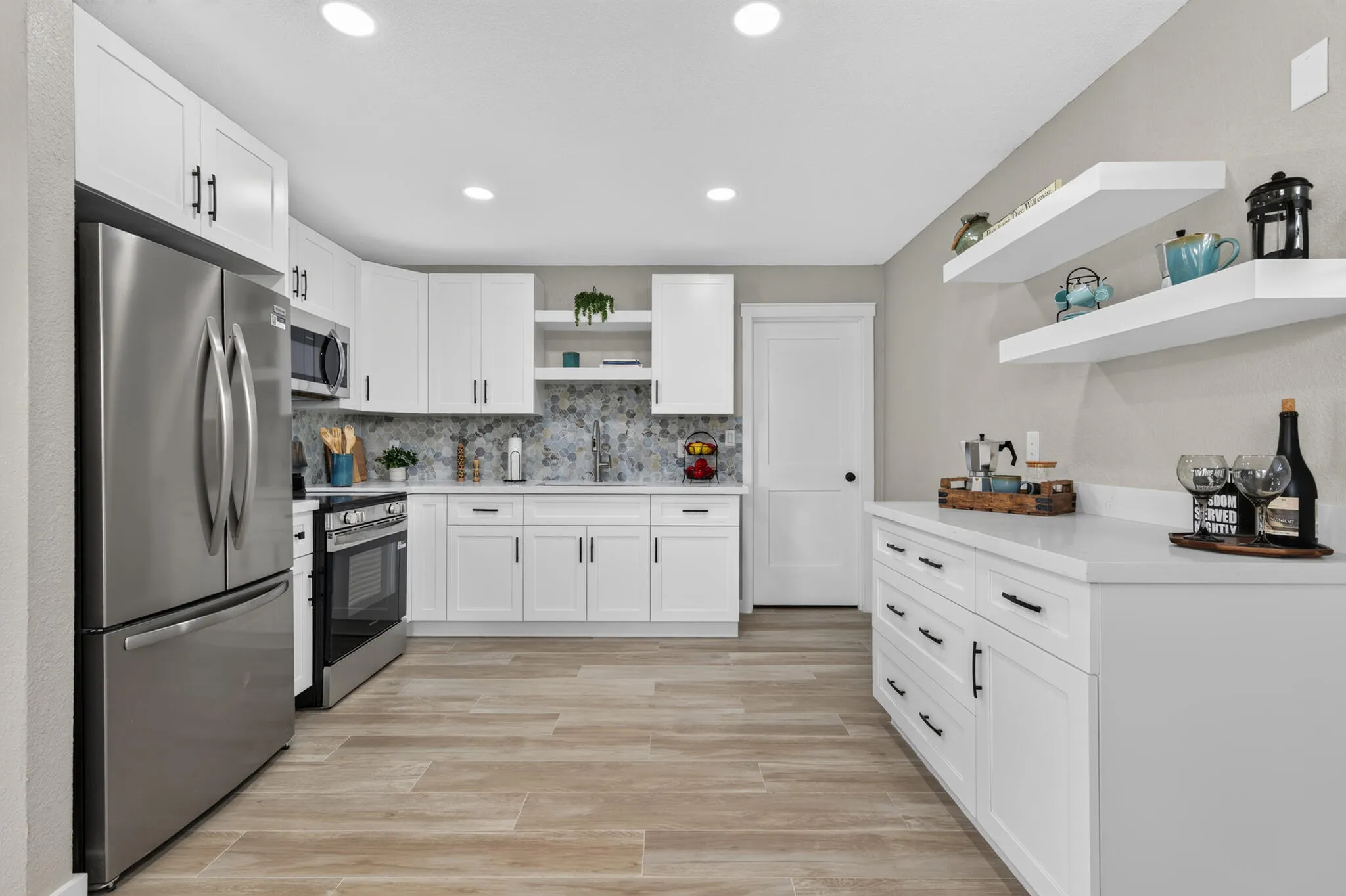 Modern kitchen featuring white shaker cabinetry, stainless steel appliances, a tile backsplash, light-toned wood-finish flooring, and a stone countertop.