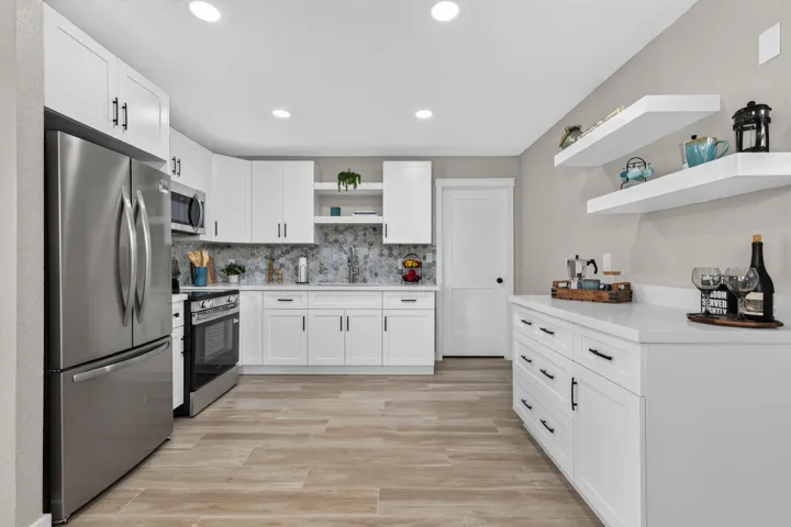 Modern kitchen featuring white shaker cabinetry, stainless steel appliances, a tile backsplash, light-toned wood-finish flooring, and a stone countertop.