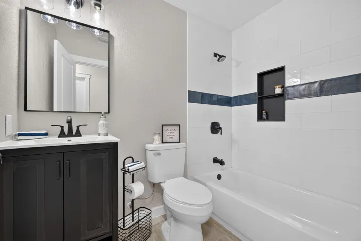 Contemporary bathroom featuring a vanity with integrated sink and matte black hardware, white subway tile walls with navy accent stripe, wood-finish flooring, and a bathtub/shower combination with tile surround and modern fixtures