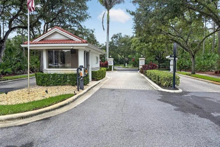 Gated entry with a guardhouse, paver driveway, and mature landscaping