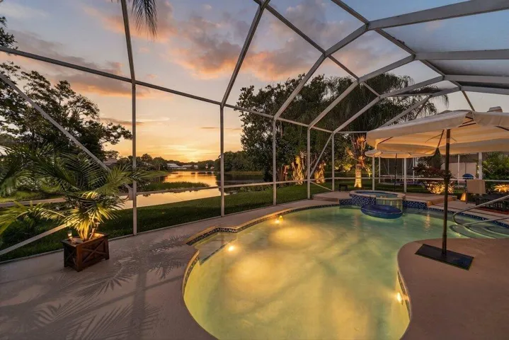 Screened-in outdoor living space featuring a custom pool, integrated spa, and direct water access