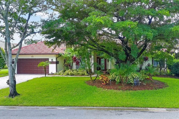 Exterior featuring a tile roof, an integrated two-car garage with a brown door, mature trees, and a landscaped front yard with varied plantings