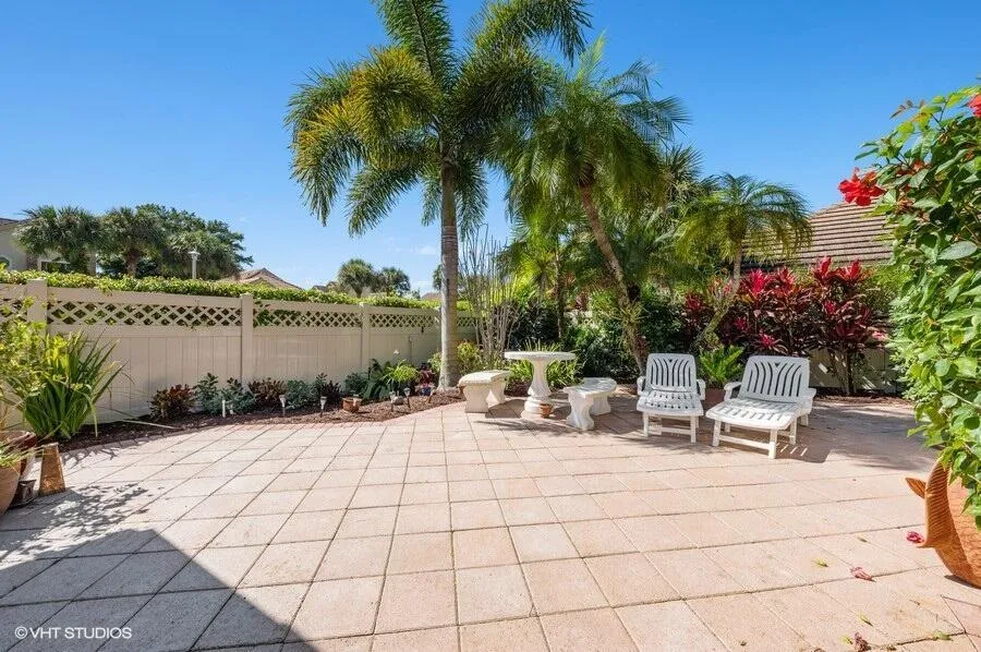 Paved patio area with tropical landscaping, privacy fencing, and mature palm trees