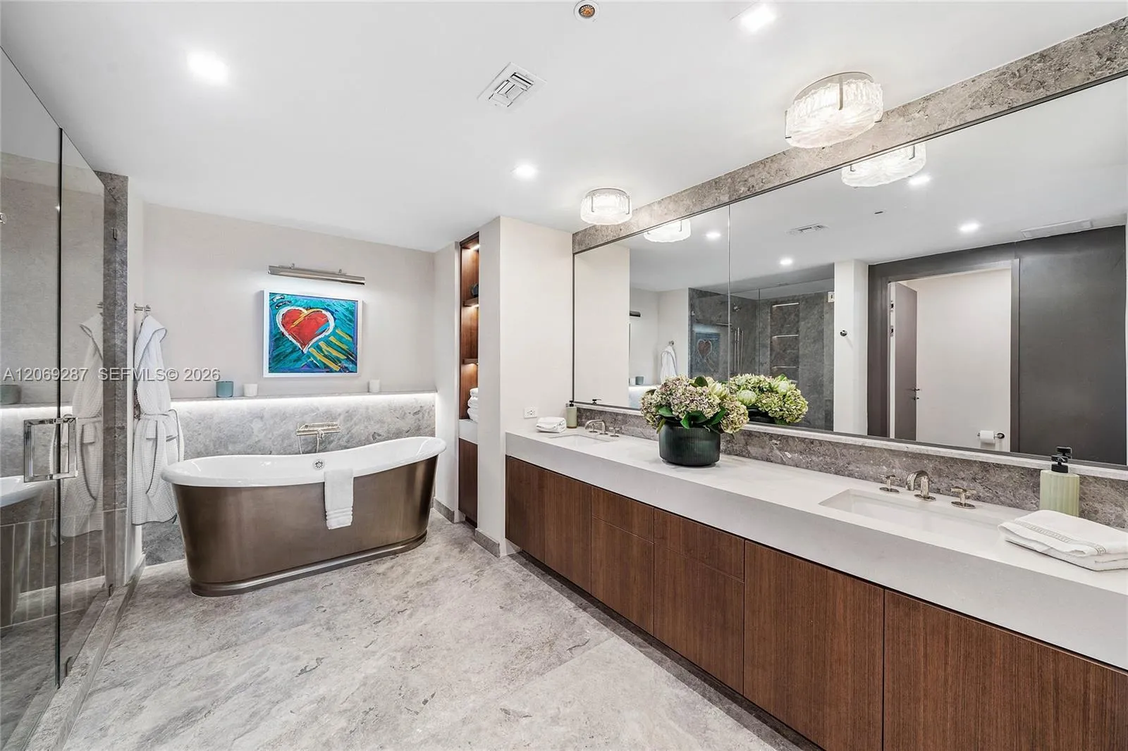 An en-suite bathroom featuring elegant finishes, dual vanities, a soaking tub and an oversized glass-enclosed shower.