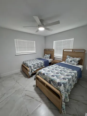 White tile flooring with grey veining, two windows with blinds, and a ceiling fan with integrated lighting