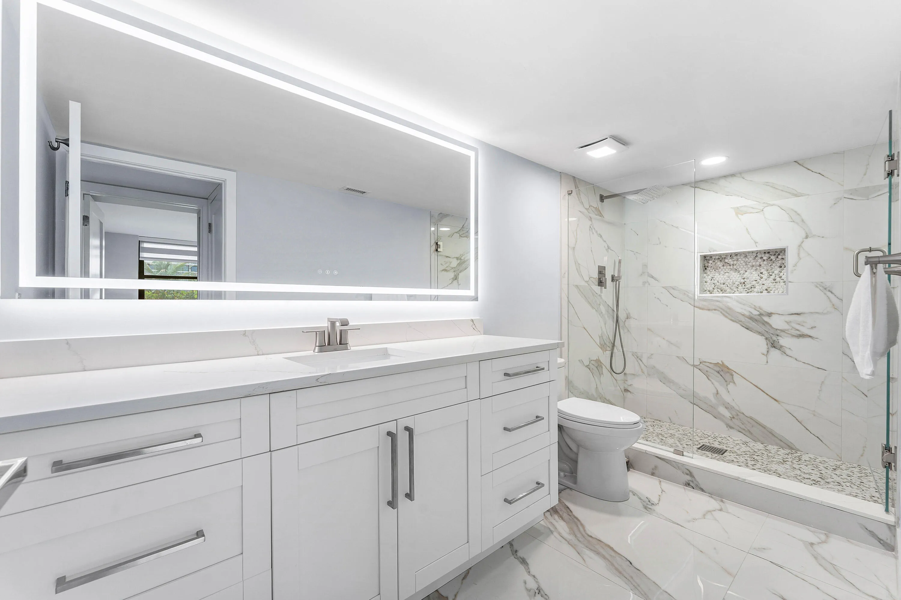 Fully renovated vanity with white shaker cabinetry, stunning large all tile and glass shower and a large illuminated mirror