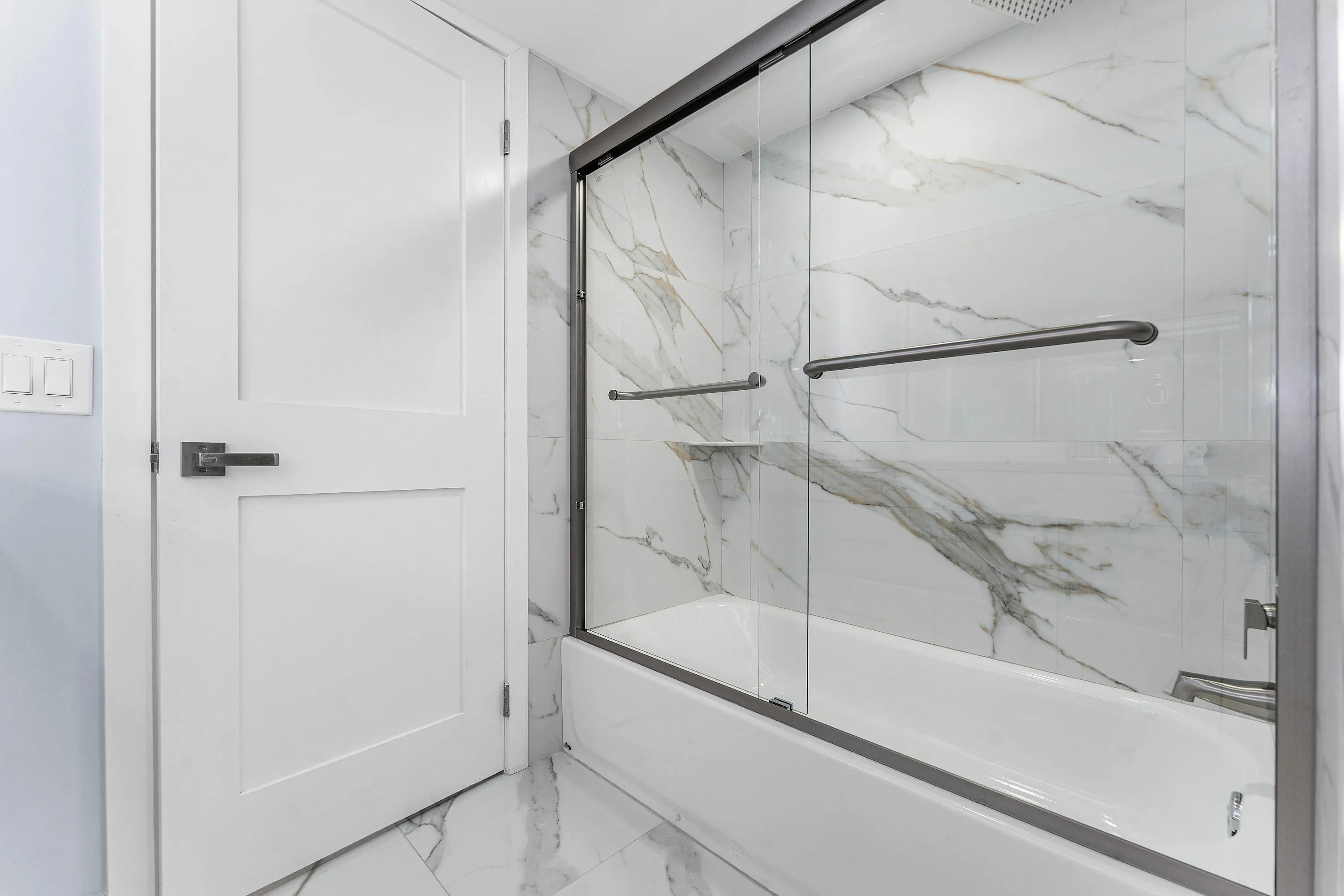 Bathtub with glass enclosure, wall tiling, and coordinating floor tiles.