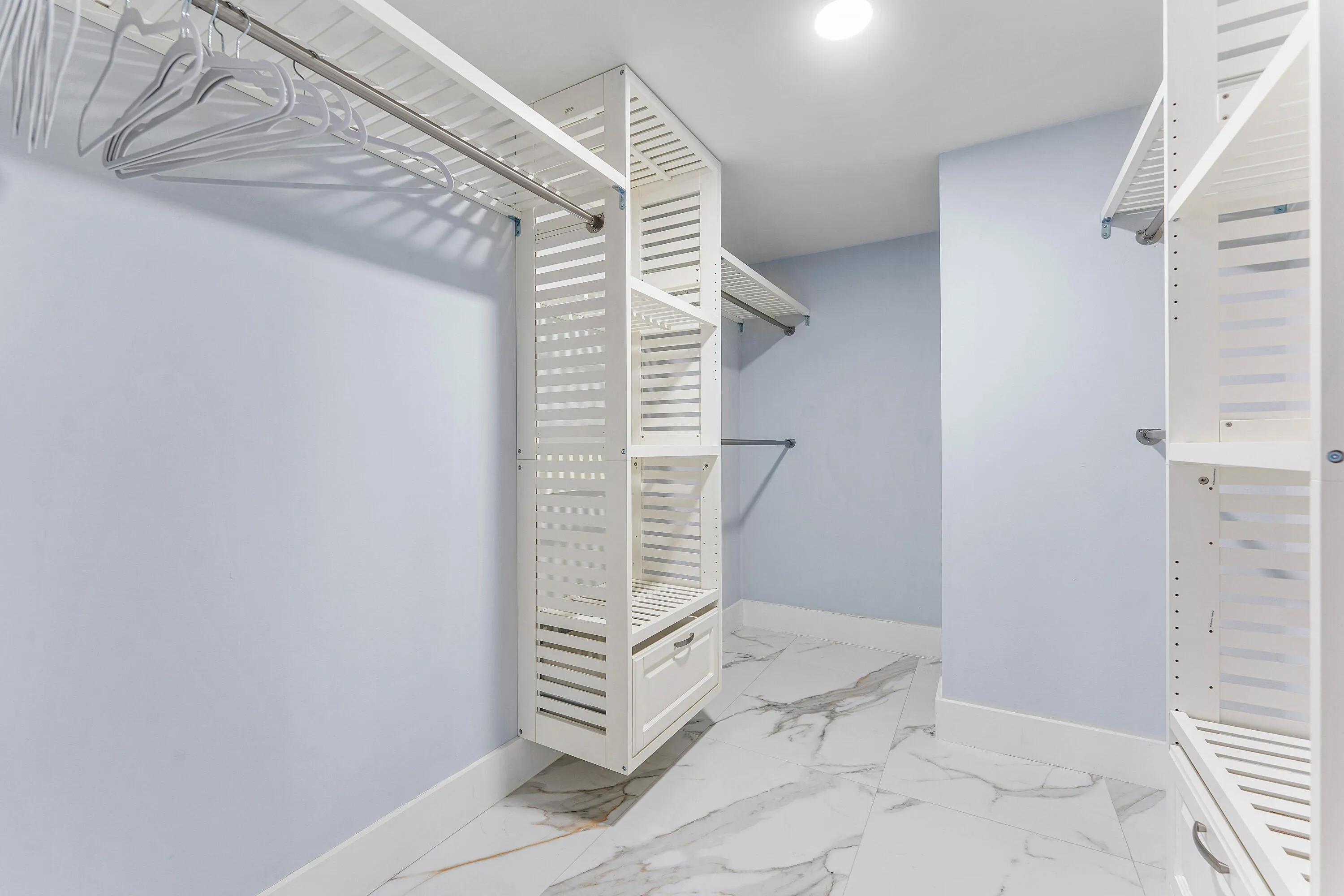 Custom closet system featuring shelving, hanging rods, and built-in drawers, complemented by large format floor tiling