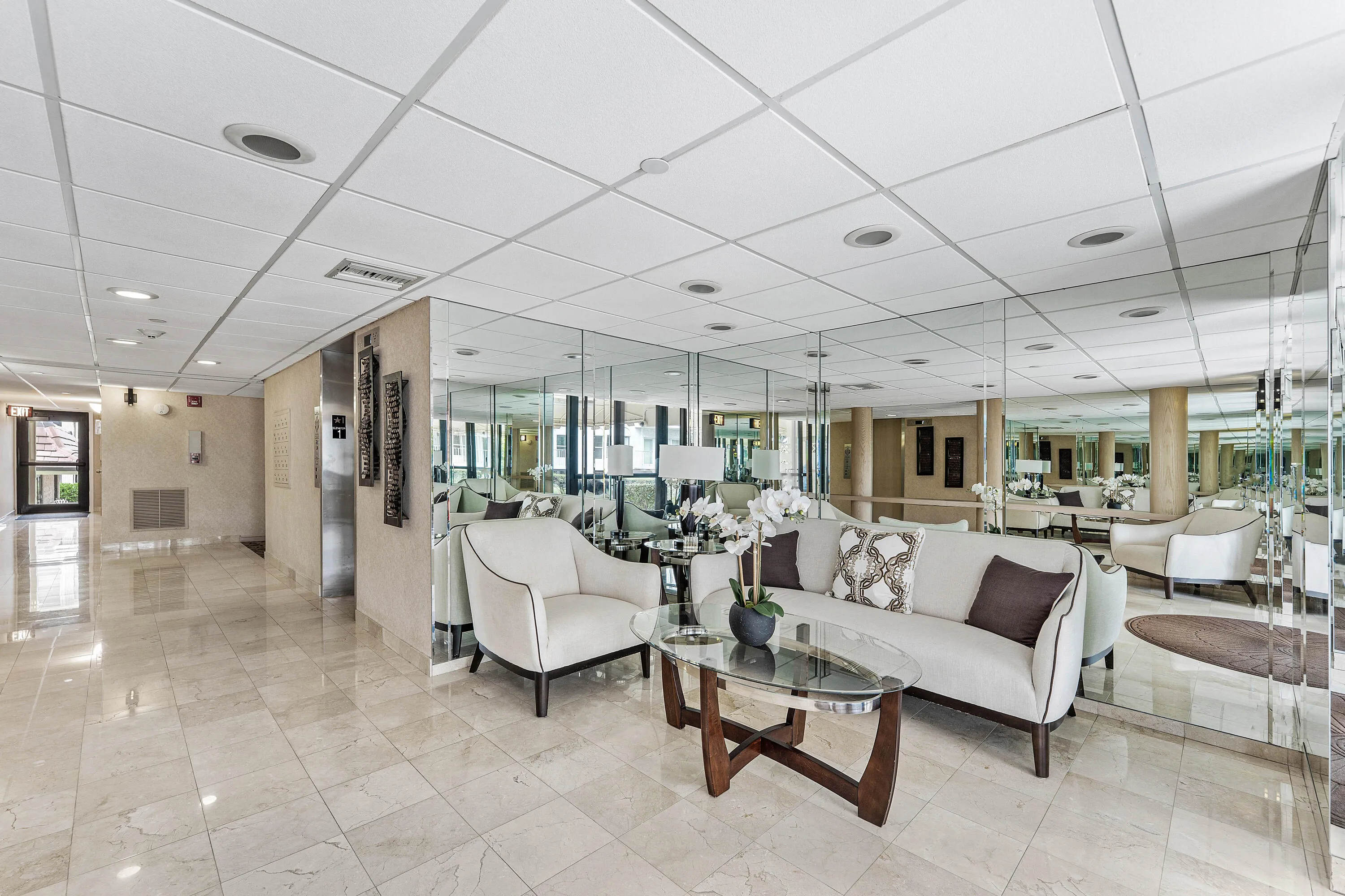 Spacious common area featuring large format tile flooring, mirrored wall accents, recessed lighting, and a suspended acoustic tile ceiling