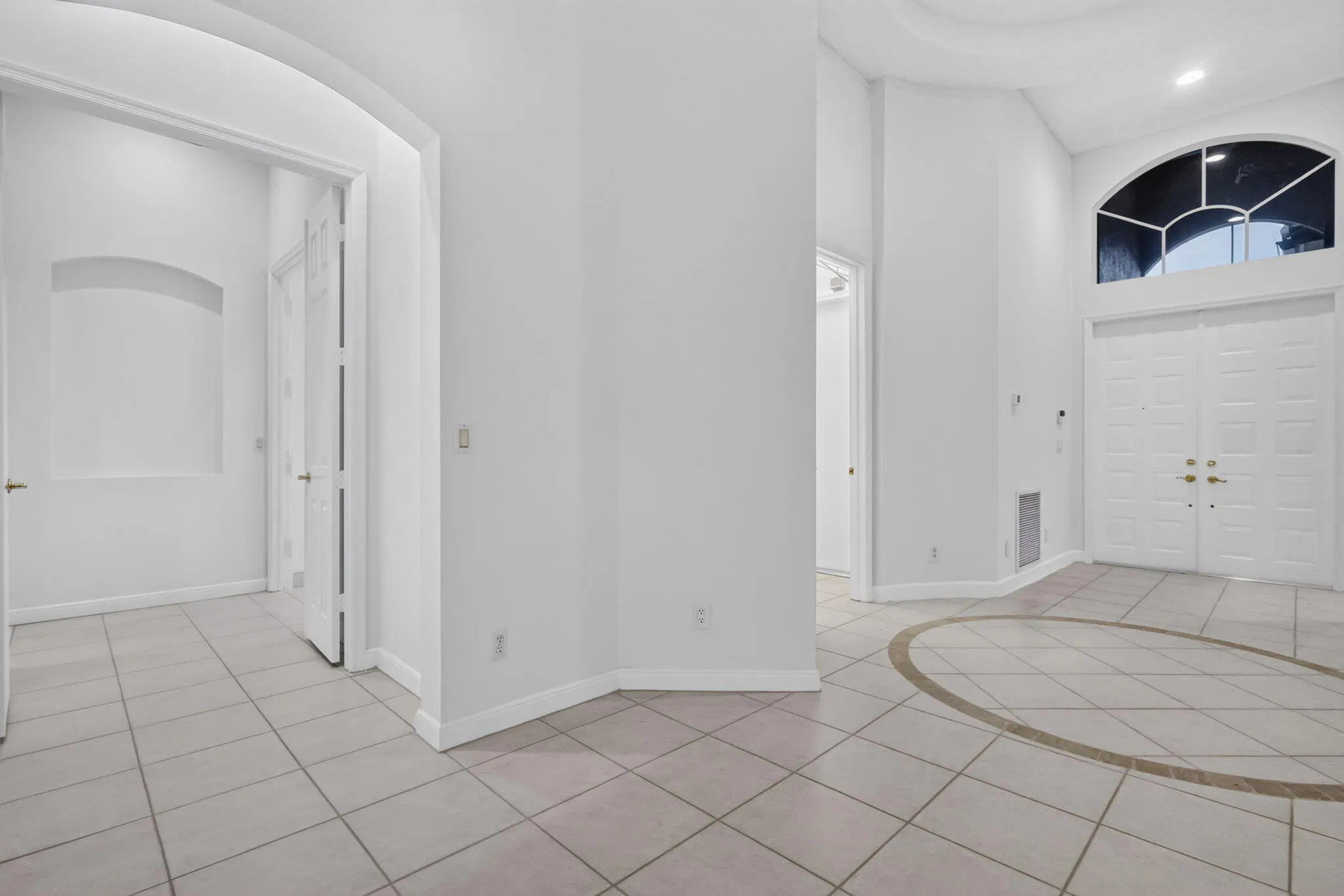 Double-door entry with an arched transom window, tile flooring with an inlaid circular design, arched doorway, and built-in wall niche