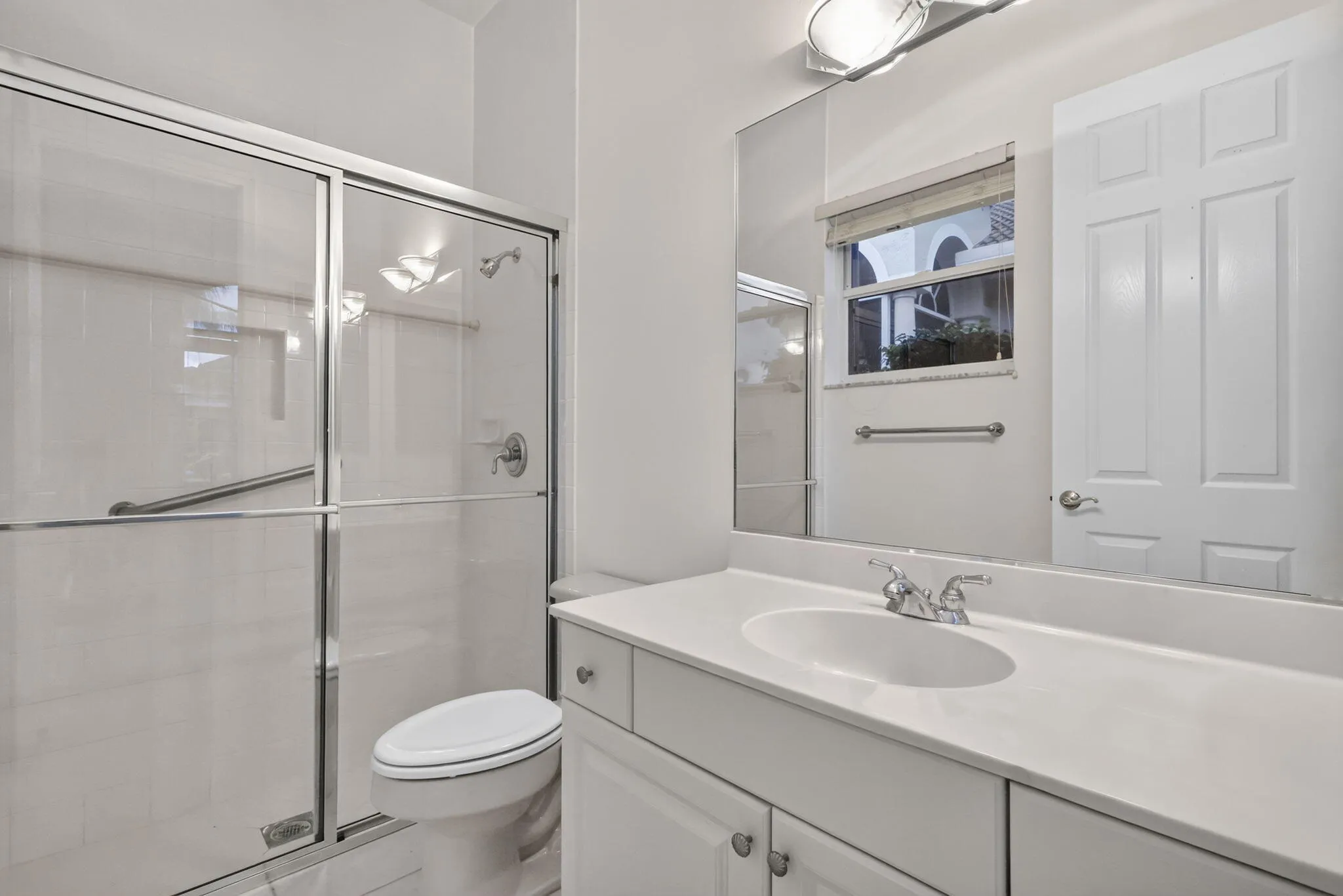 Glass-enclosed shower with a grab bar, single vanity with an integrated sink, white cabinetry, and a framed mirror