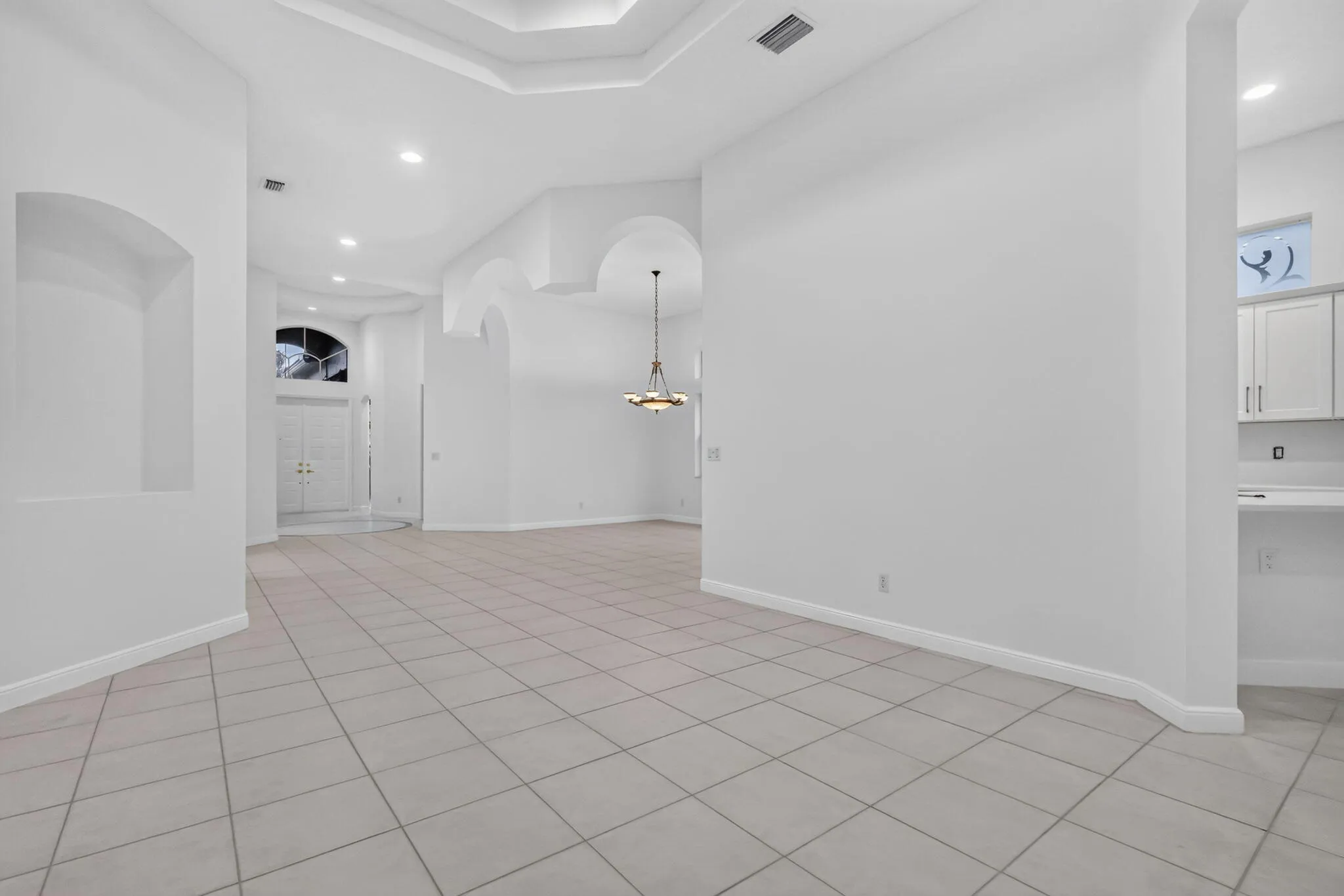 Recessed lighting, arched doorways, tiled flooring, built-in wall niche, and a tray ceiling with crown molding