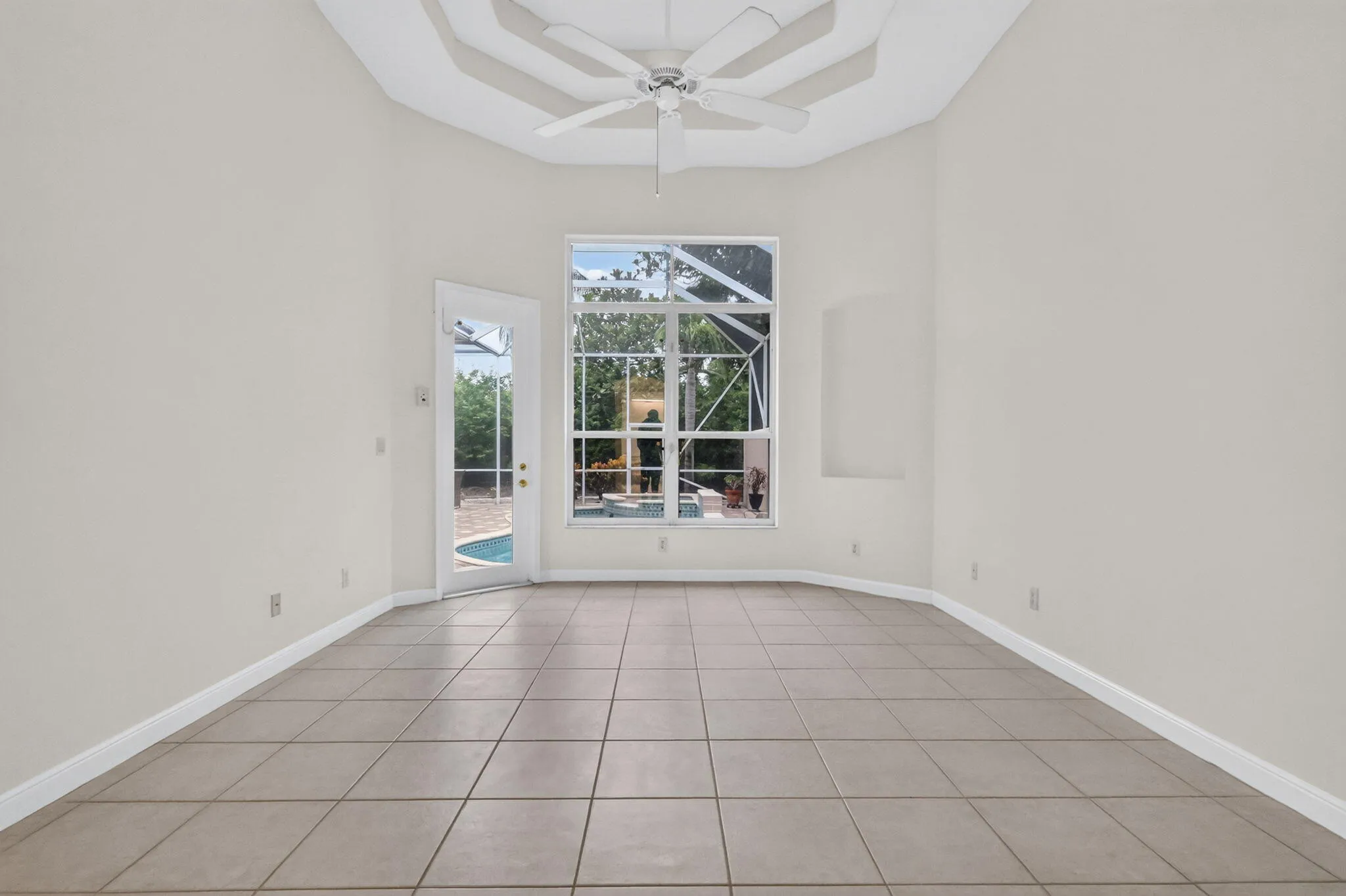 Recessed ceiling with ceiling fan, tile flooring, large window, and glass-paneled door