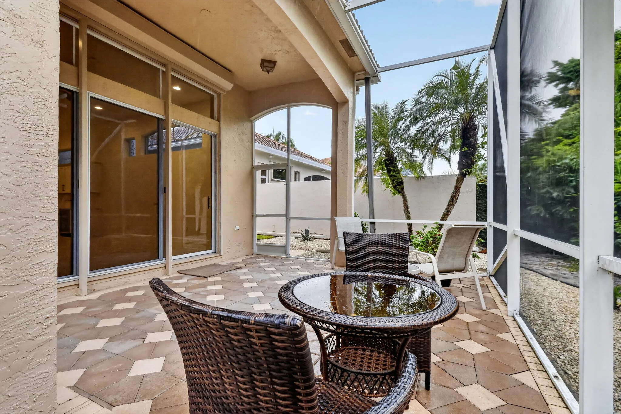 Screened lanai featuring patterned paver flooring, stucco exterior, and large sliding glass doors