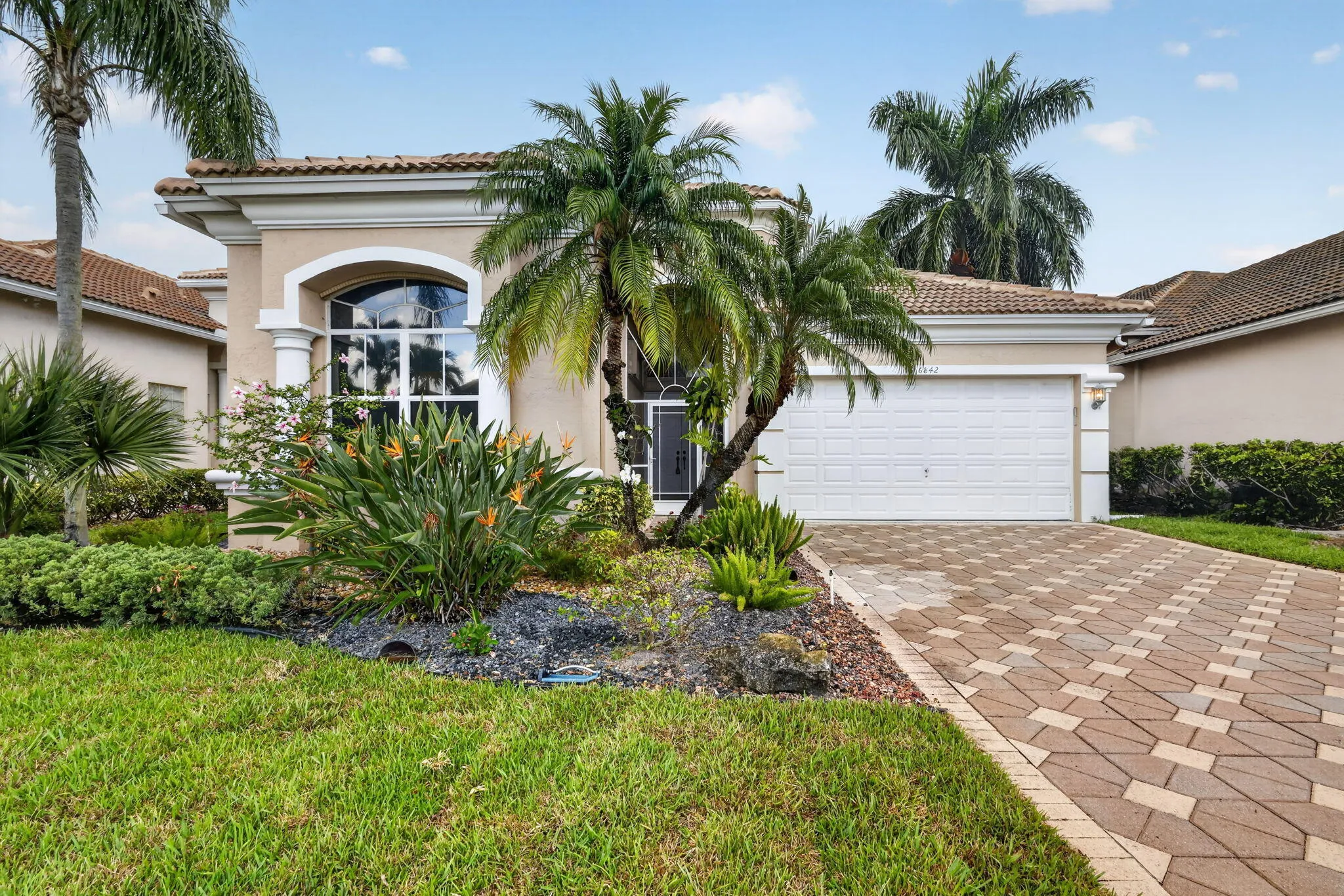 Stucco exterior with a tile roof, arched window, attached two-car garage, and a paver driveway