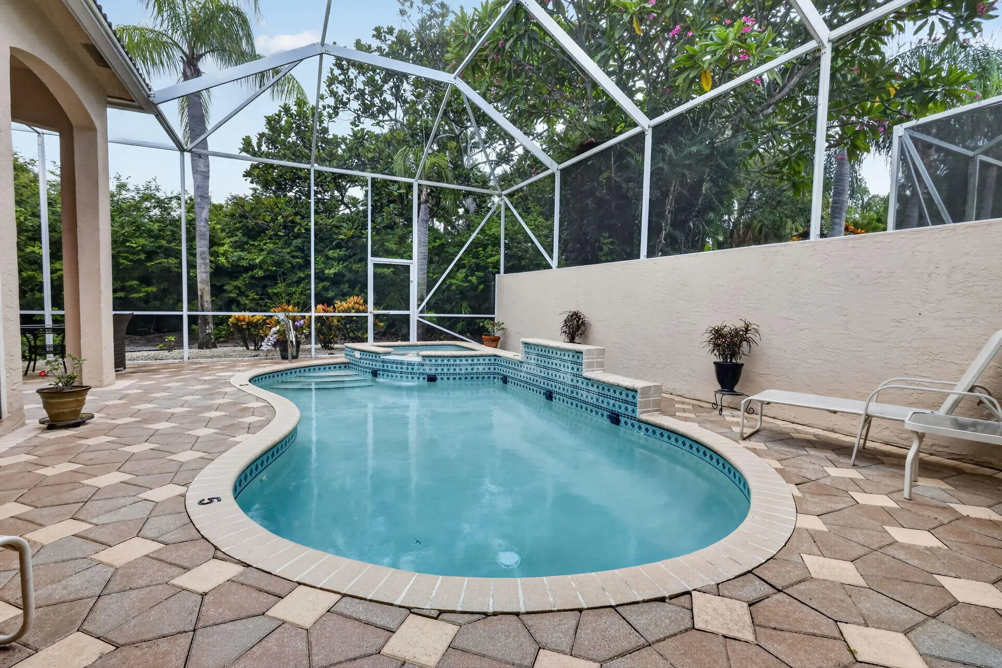 Screened enclosure featuring a freeform pool with integrated spa and decorative tile