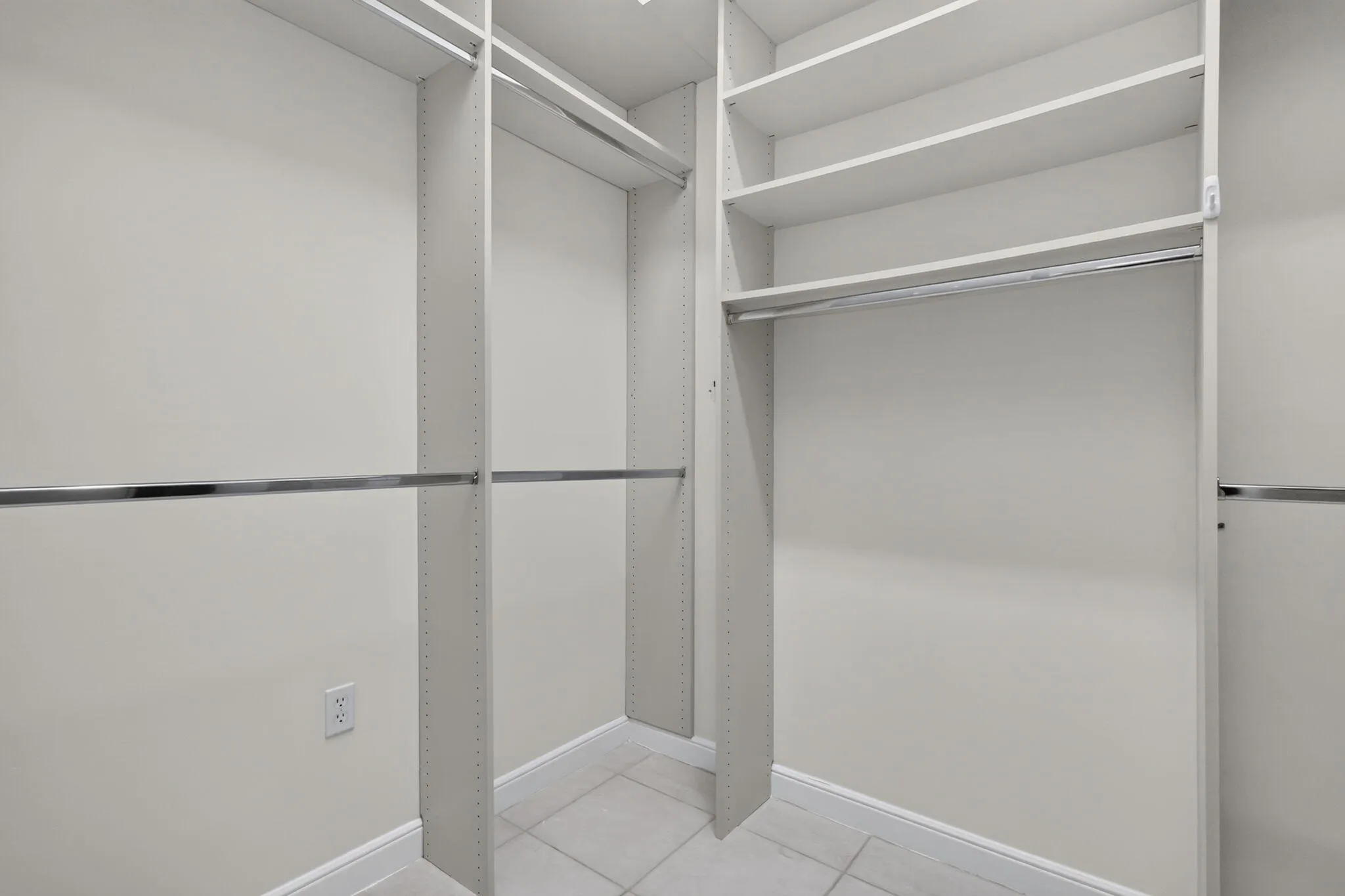 Custom closet system with white shelving, chrome hanging rods, and light-toned tile flooring