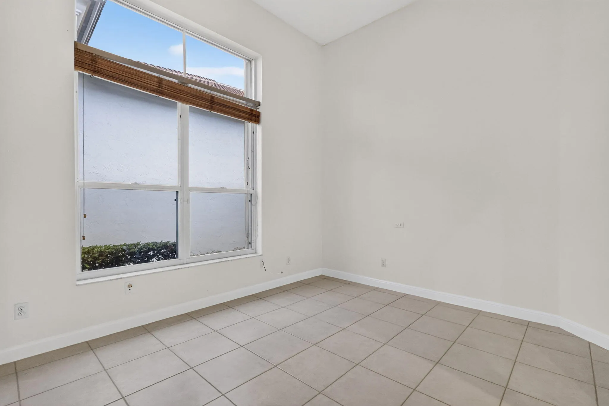 Bright room featuring a large window, neutral tile flooring, and white walls