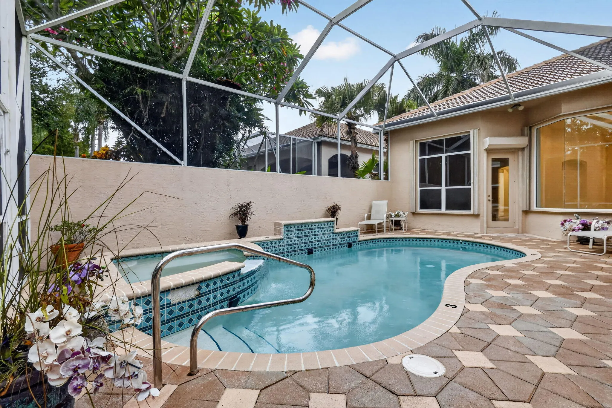 Freeform swimming pool with integrated spa and tiled accents, screen enclosure, paver patio, and stucco exterior