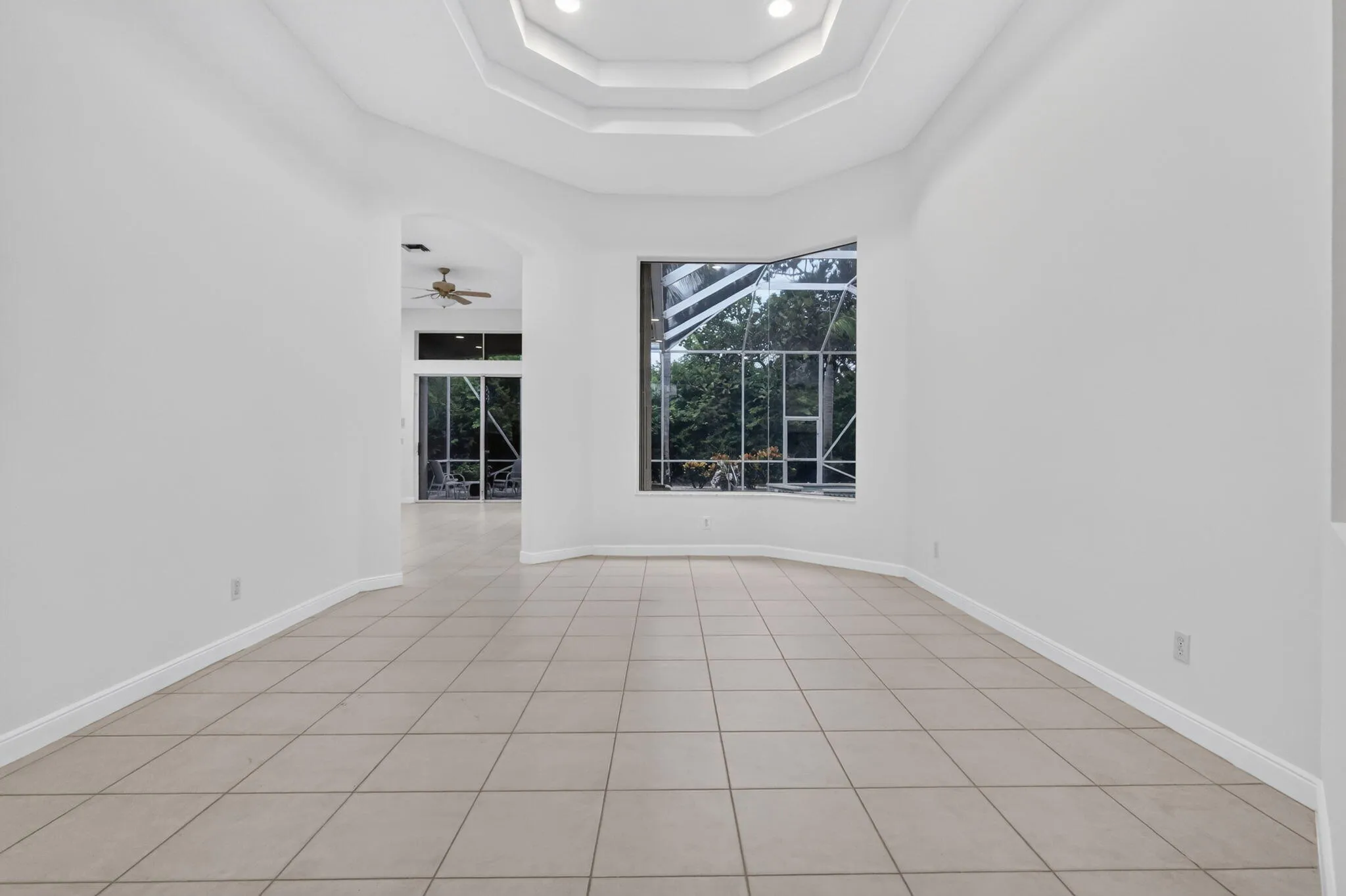Recessed lighting in a tiered tray ceiling, large windows, and neutral-toned tile flooring