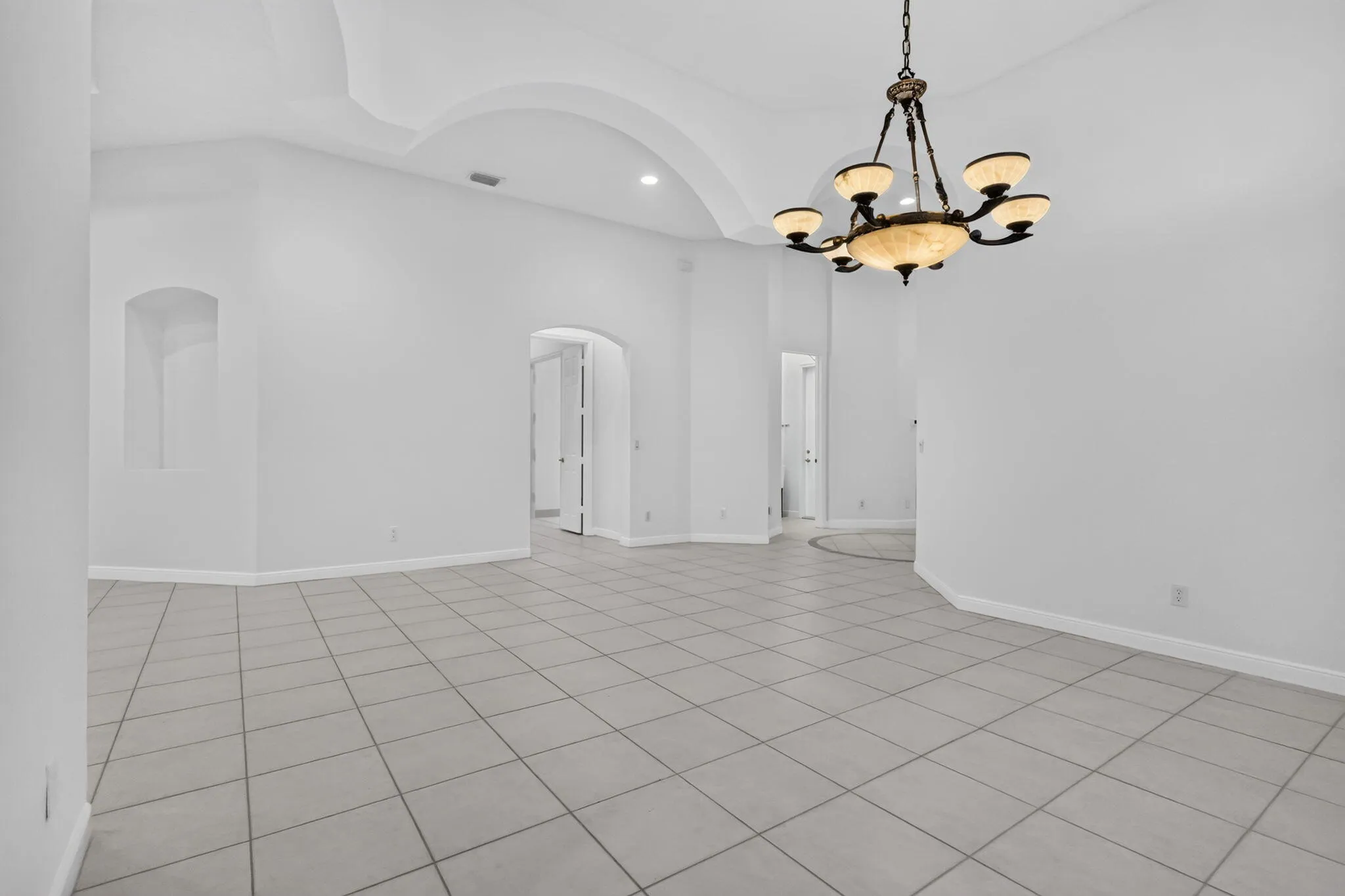 Arched doorways, recessed ceiling details, and a built-in wall niche complement the tiled flooring and multi-light chandelier